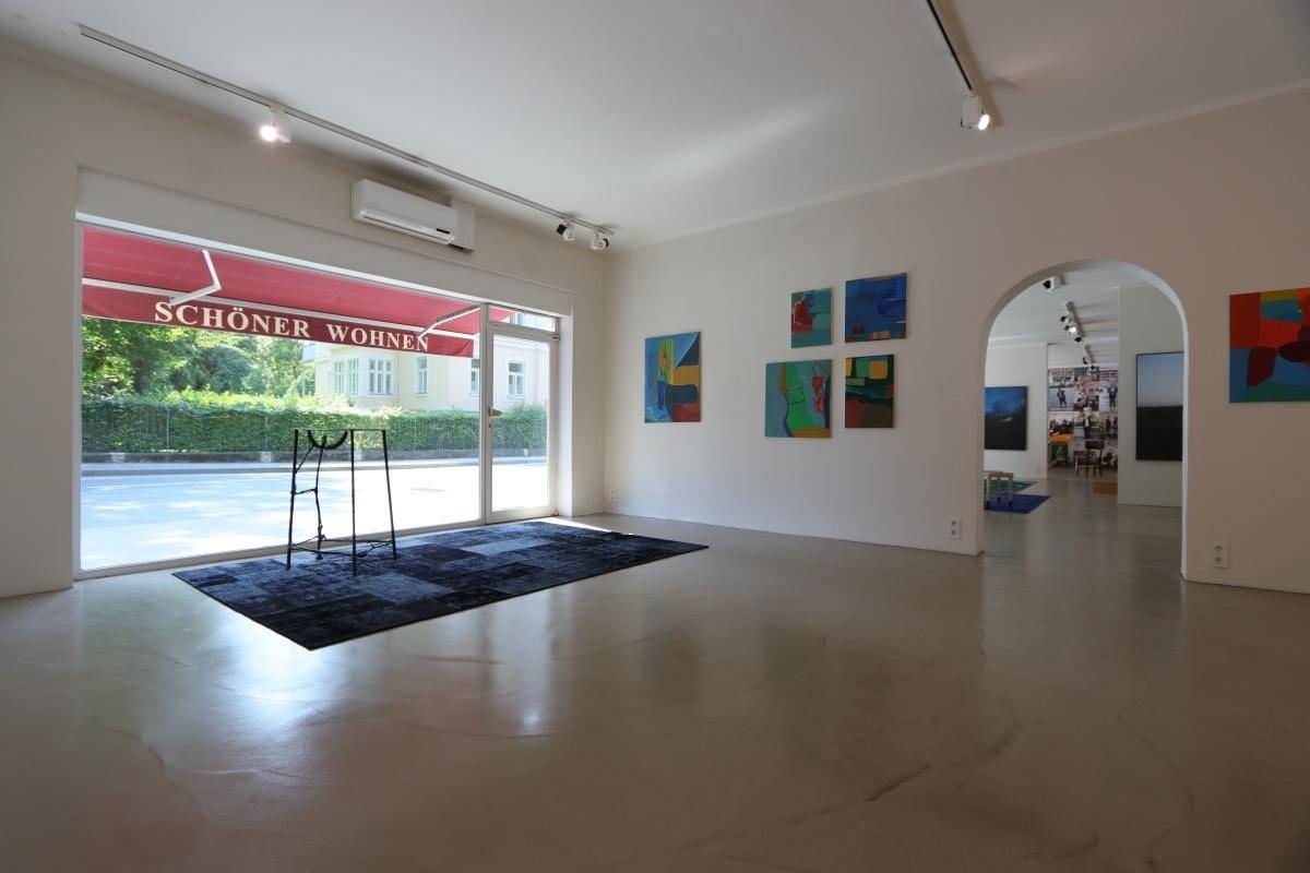 Heller Ausstellungsraum mit großen Schaufenstern, Klimaanlage und moderner Kunst an den Wänden.