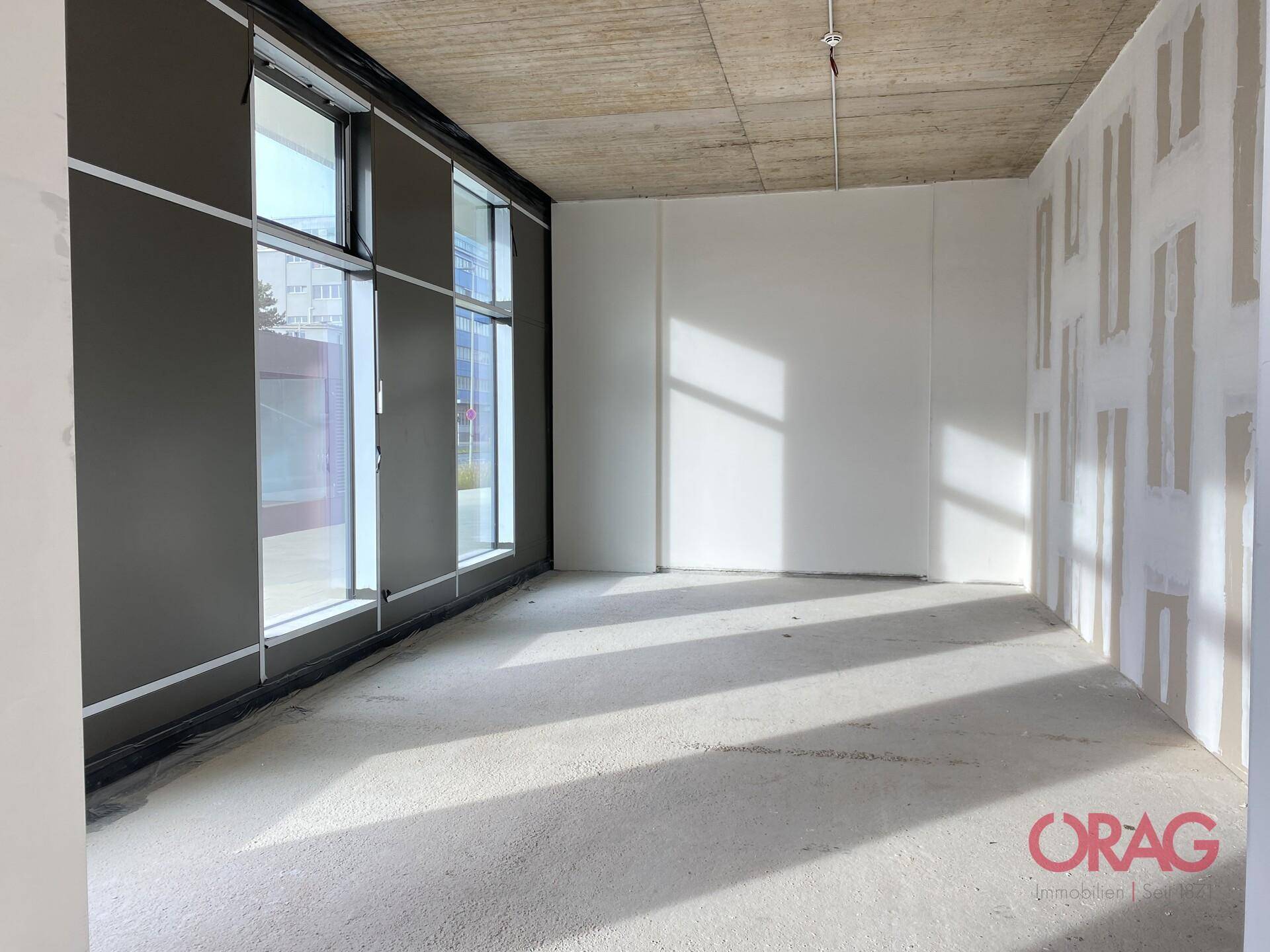 Unfertiger Gewerberaum mit großen Fenstern und viel Tageslicht, bereit für den Innenausbau.