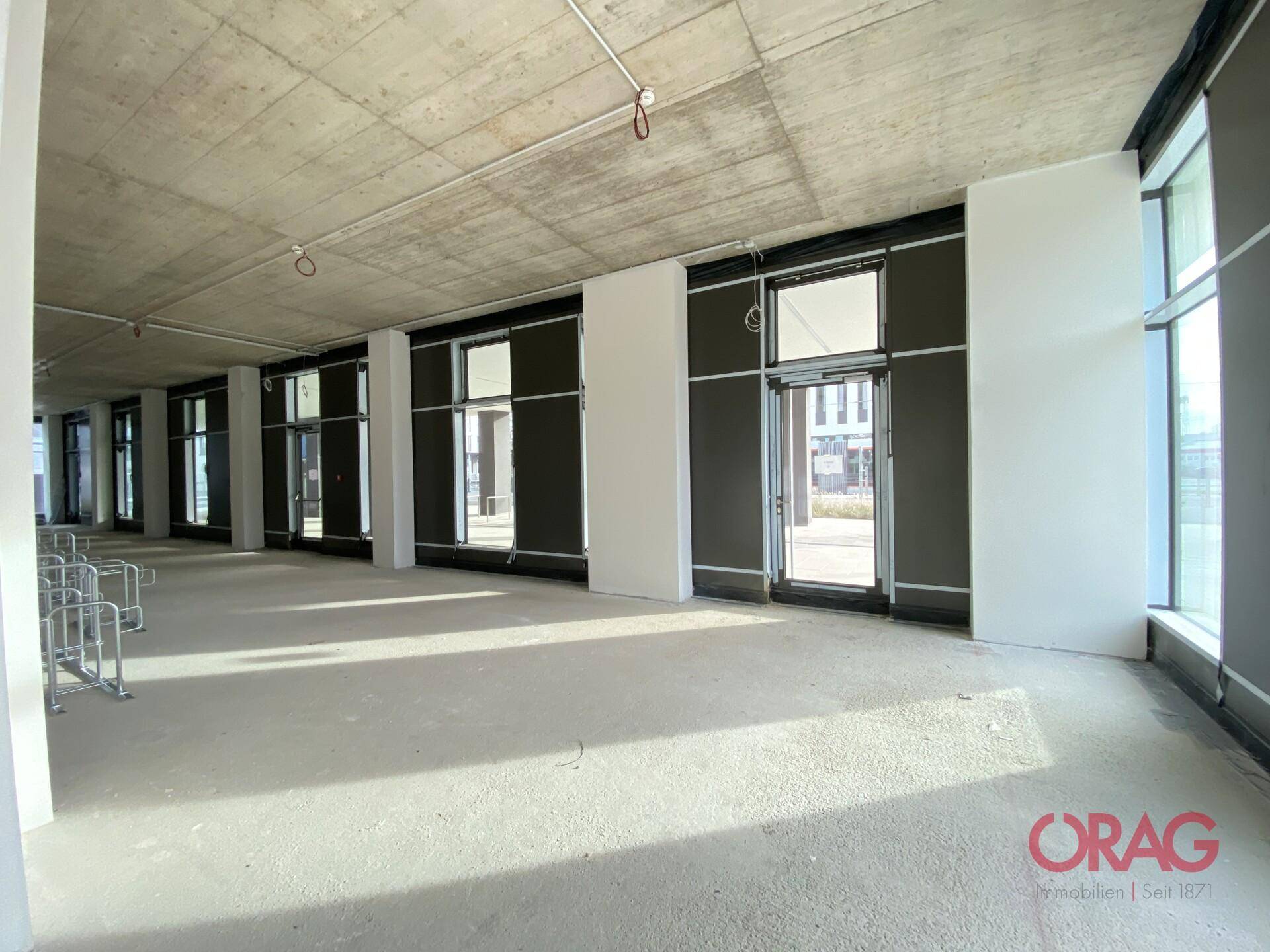 Heller Gewerberaum mit großen Fenstern und Zugang zur Straße, im Rohbauzustand für flexible Nutzung.
