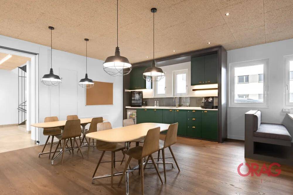 Helle Gemeinschaftsküche mit dunklen Schränken, Holzboden und mehreren Esstischen für Mitarbeiter.