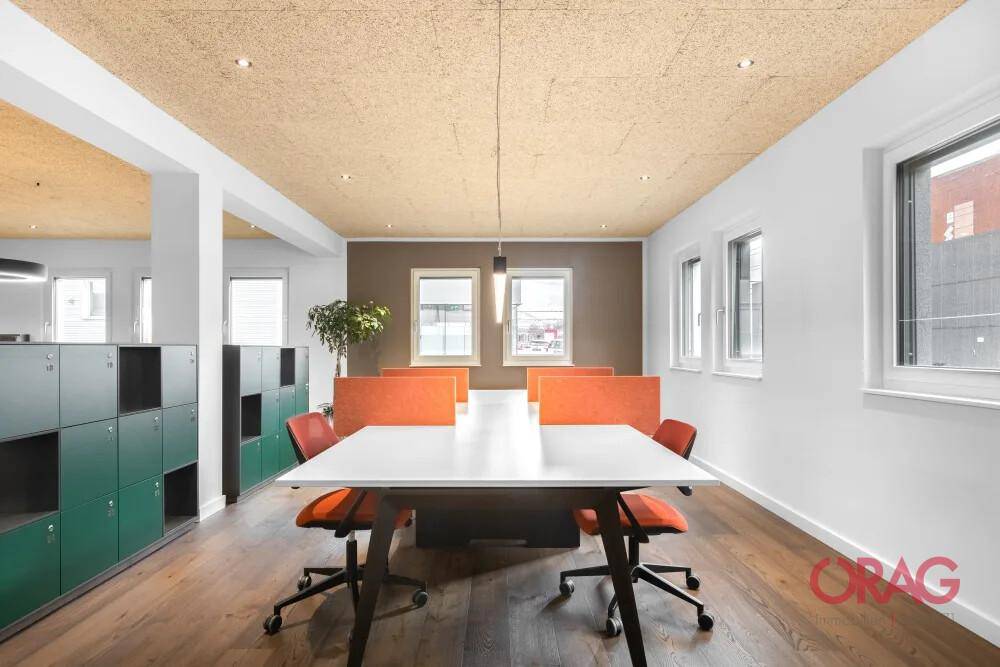 Offener Bürobereich mit Holzboden, Akustikdecke und modernen Arbeitsplätzen mit farbigen Trennwänden.