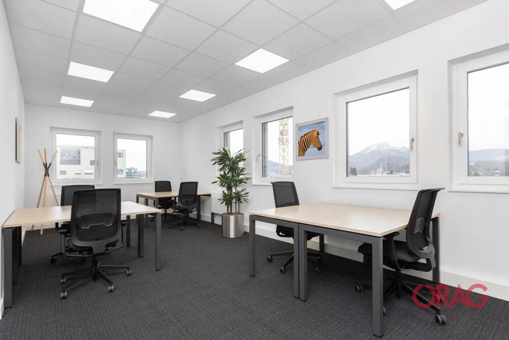 Helles Büro mit Teppichboden, großen Fenstern und mehreren Arbeitsplätzen mit Blick auf die Berge.