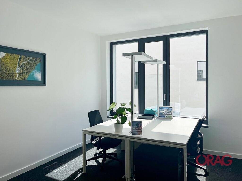 Helles Einzelbüro mit Schreibtisch, Bürostühlen und großen Fenstern für viel Tageslicht.