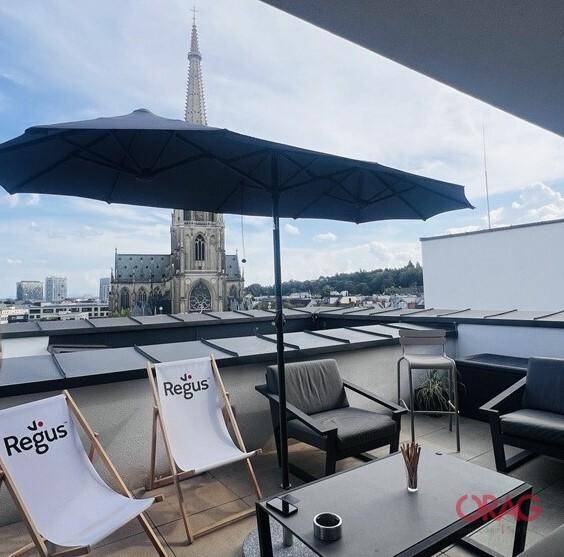 Dachterrasse mit Lounge-Möbeln, Sonnenschirm und Blick auf eine historische Kirche.