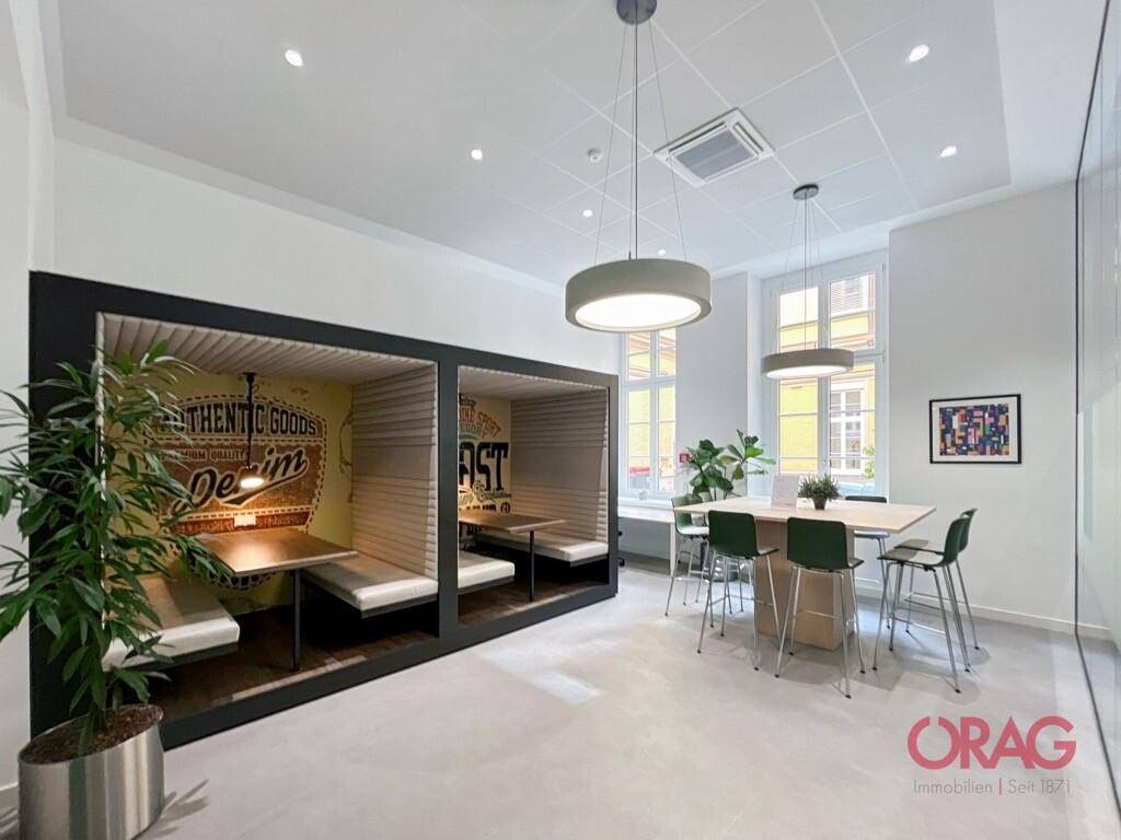 Moderner Bürobereich mit kreativen Sitznischen, großem Tisch und hellen Fenstern.