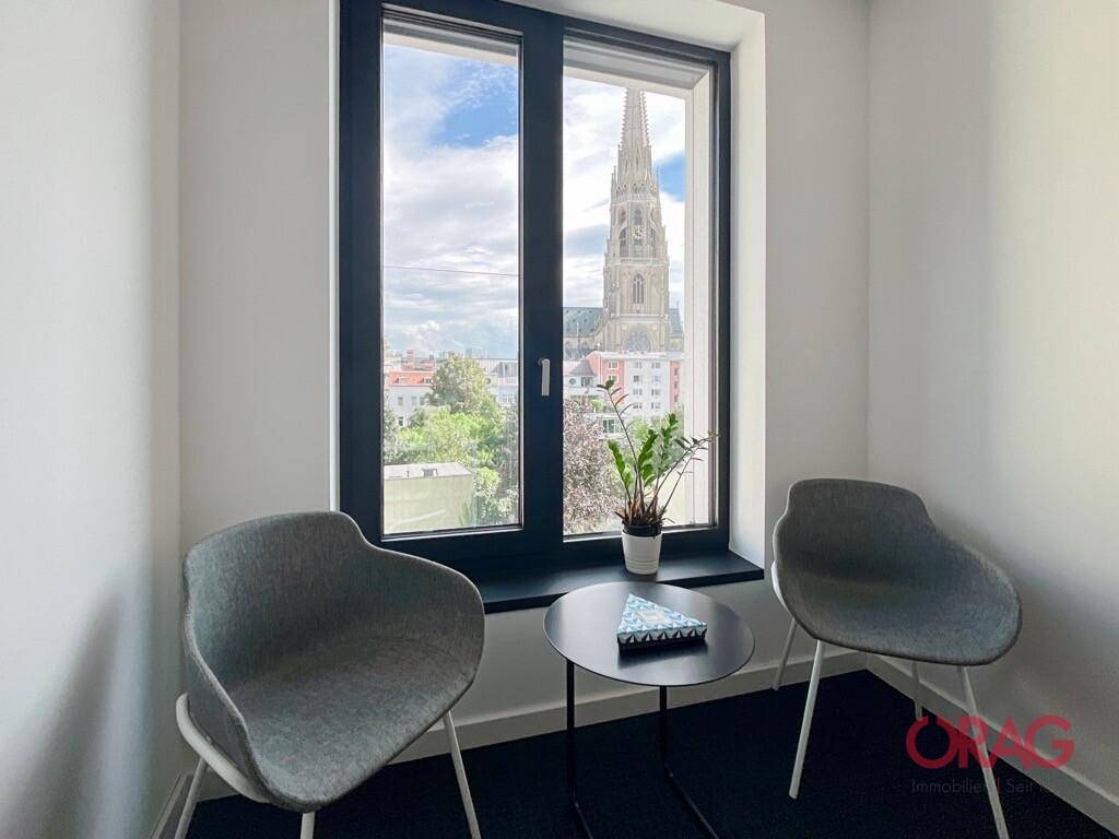 Kleiner Büroraum mit zwei Stühlen, Beistelltisch und Blick auf eine Kirchturmspitze.