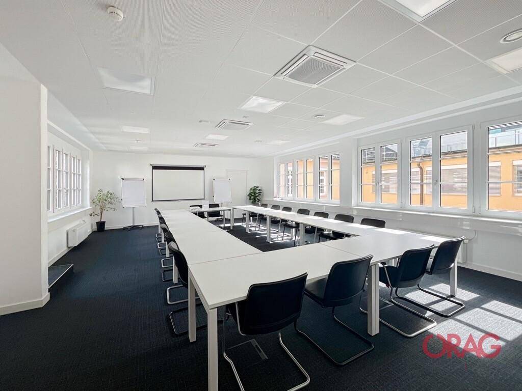 Großer Konferenzraum mit U-förmiger Tischordnung, Projektionsfläche und vielen Fenstern.