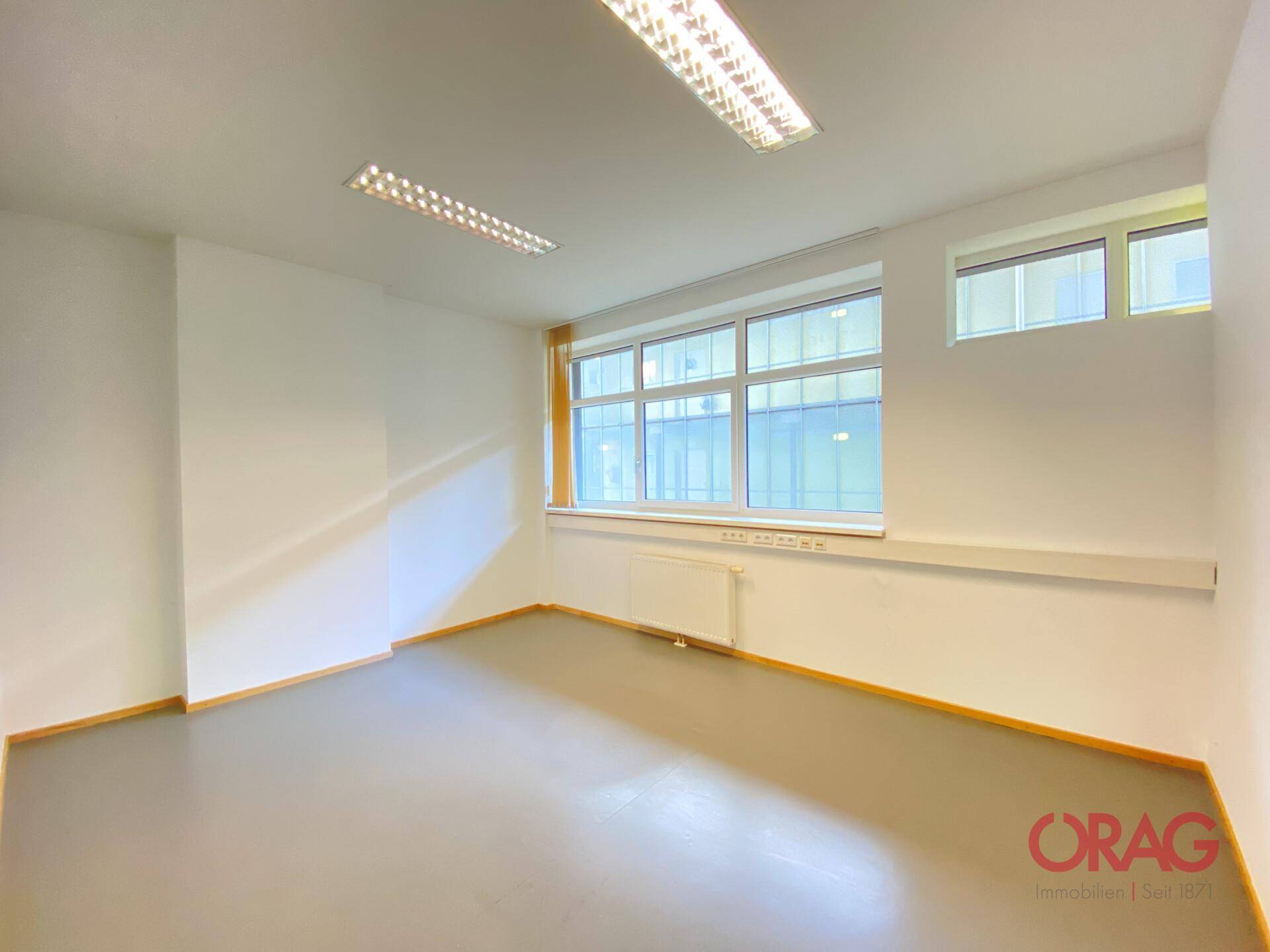 Leeres Büro mit viel Tageslicht durch große Fenster und einem schlichten, funktionalen Design.