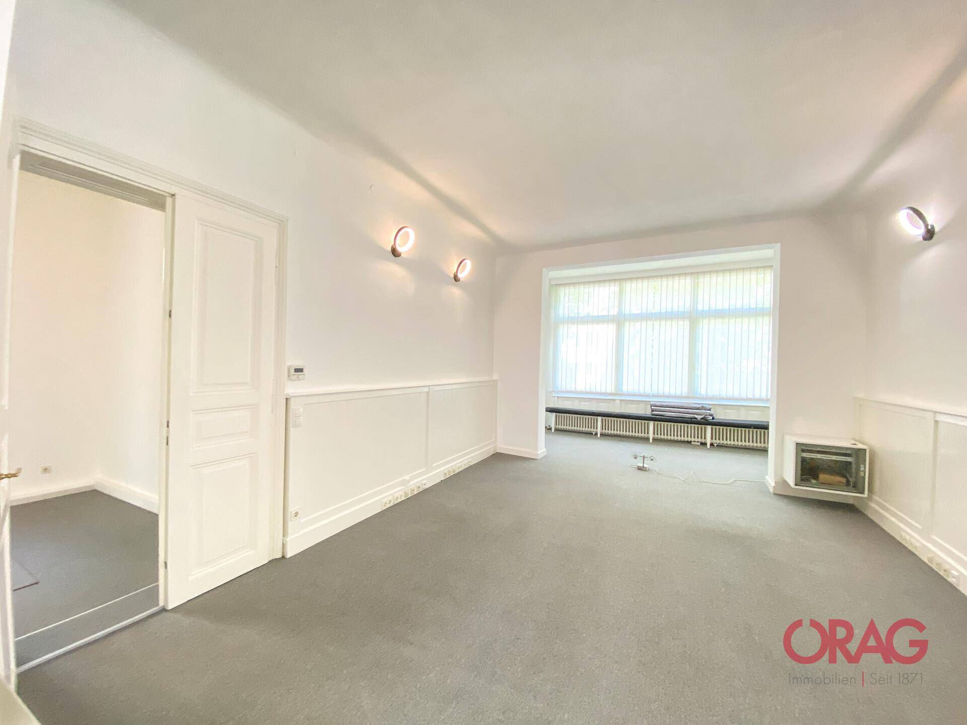Wohnraum mit Teppichboden, großen Fenstern, Wandleuchten und einem dekorativen Kamin.