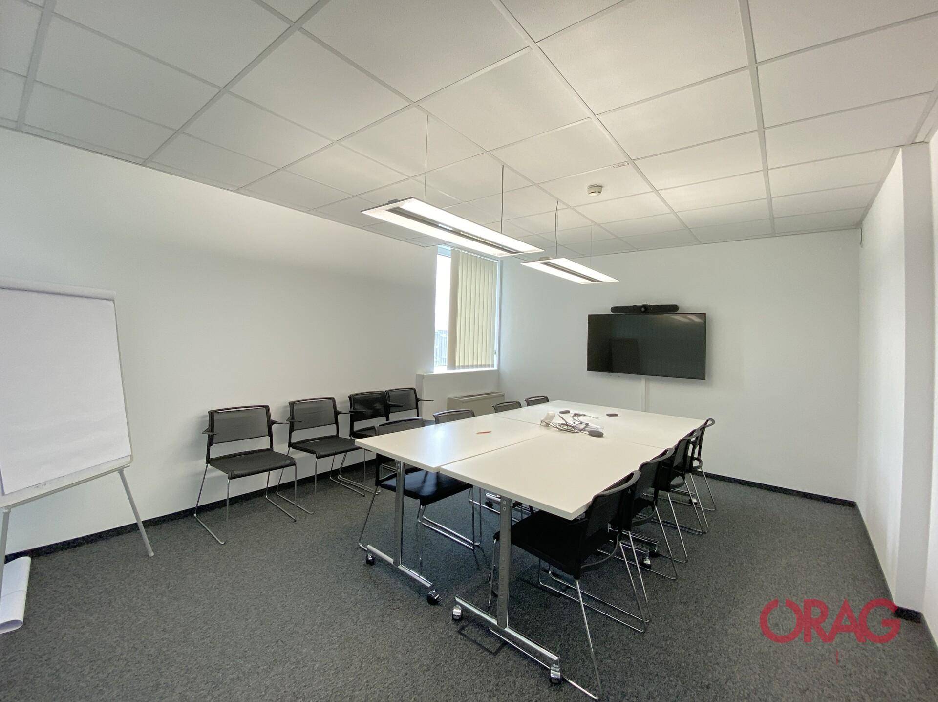 Funktionaler Konferenzraum mit großem Bildschirm, Whiteboard und flexiblem Tisch für Besprechungen.
