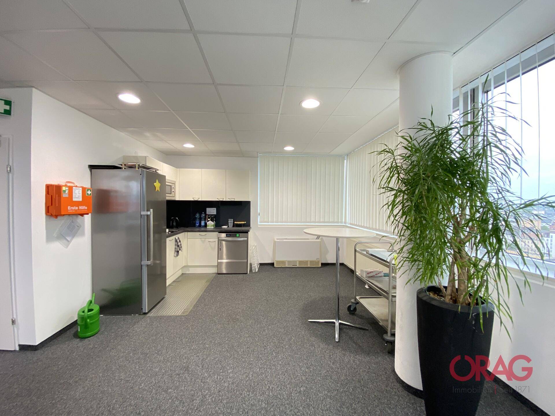 Funktionale Büroküche mit Edelstahlgeräten, weißen Schränken und großem Fenster.