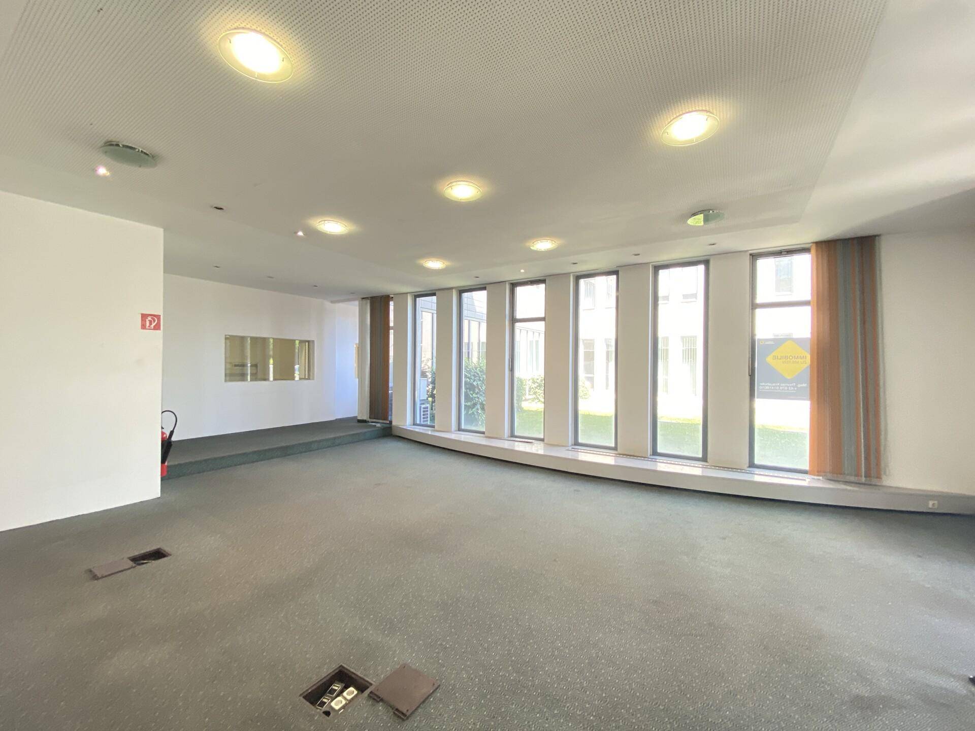 Heller Bürobereich mit Teppichboden und einer Reihe von Fenstern, die den Raum mit Licht füllen.