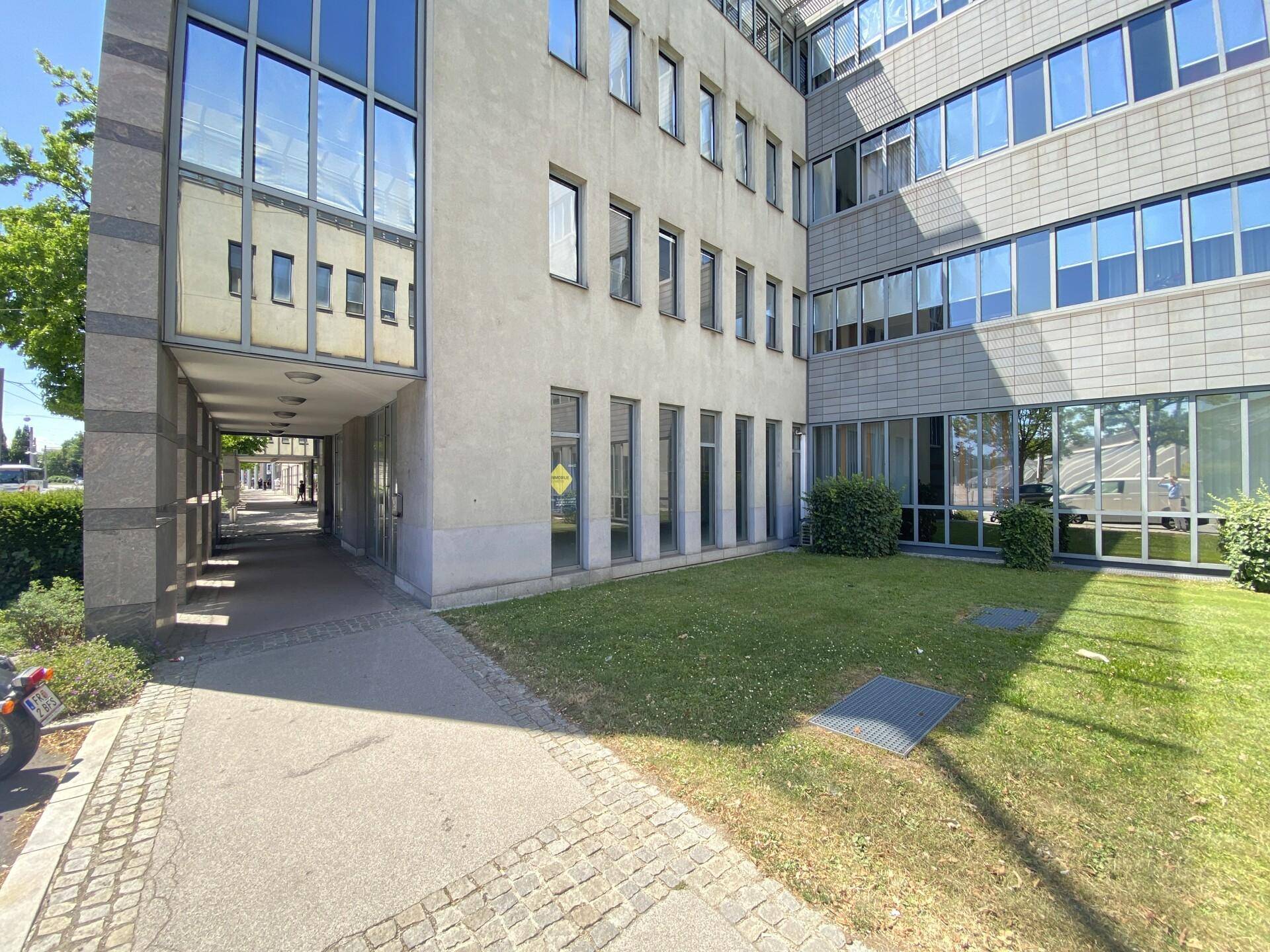 Moderne Bürogebäude-Fassade mit großen Glasflächen und einem gepflegten Rasenbereich davor.