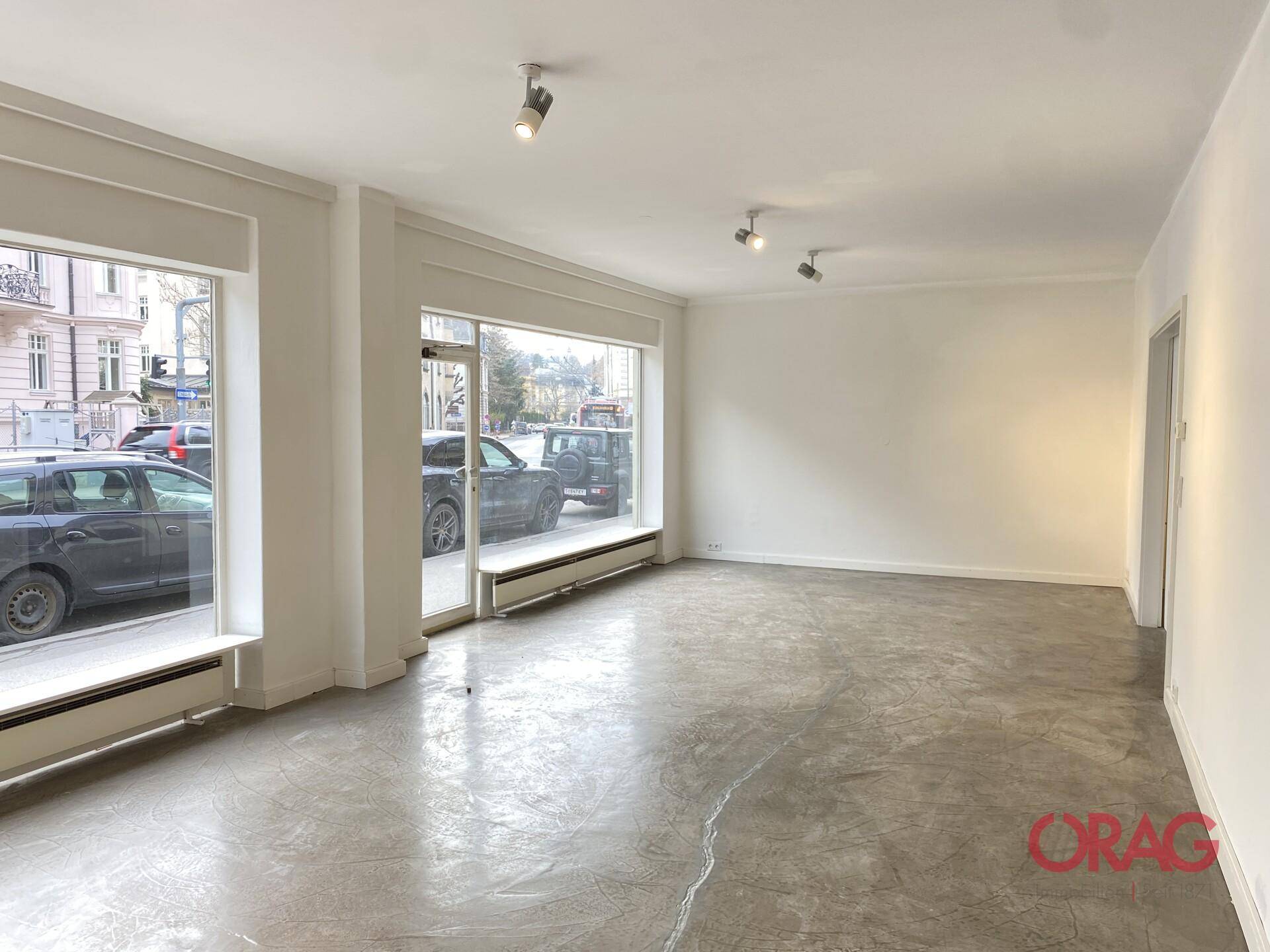 Geräumiger, leerer Ladenbereich mit großen Fensterfronten und viel Tageslicht.