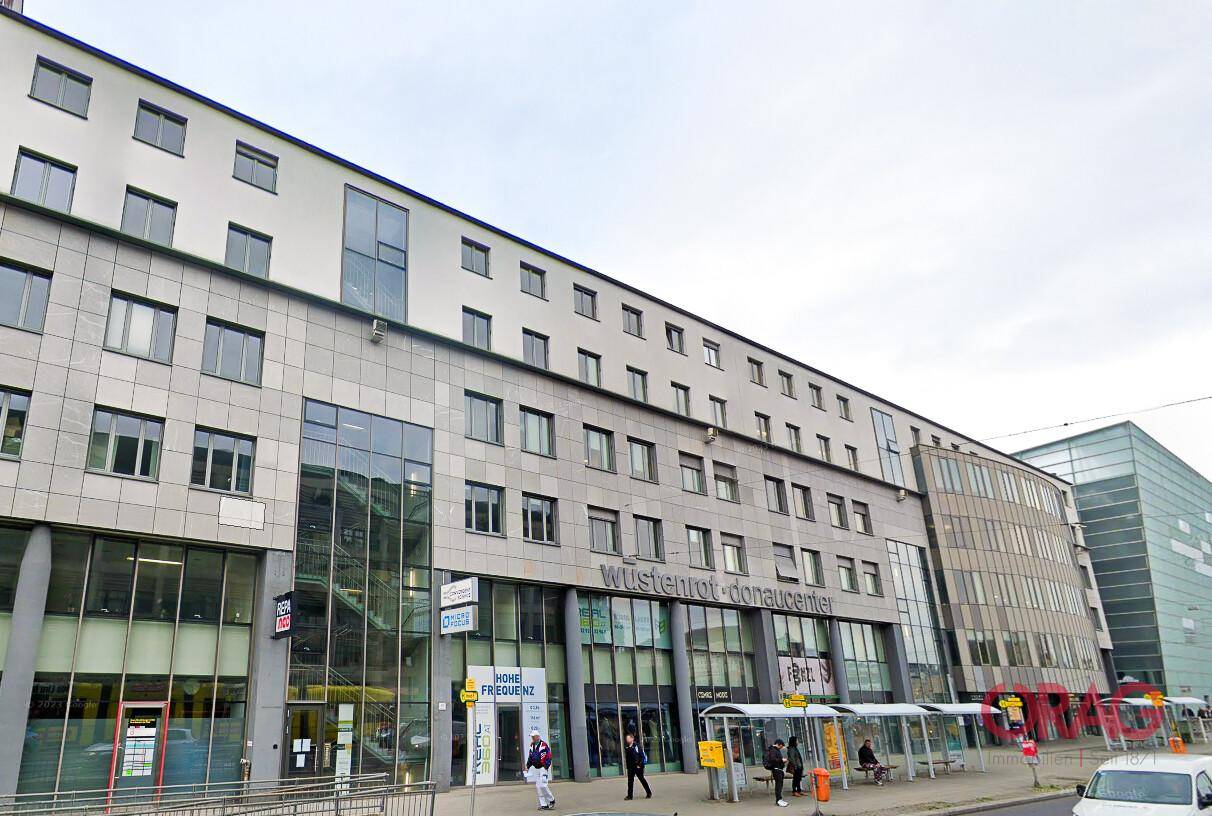 Moderne Geschäfts- und Wohngebäude mit großen Glasflächen und belebter Straßenszene.
