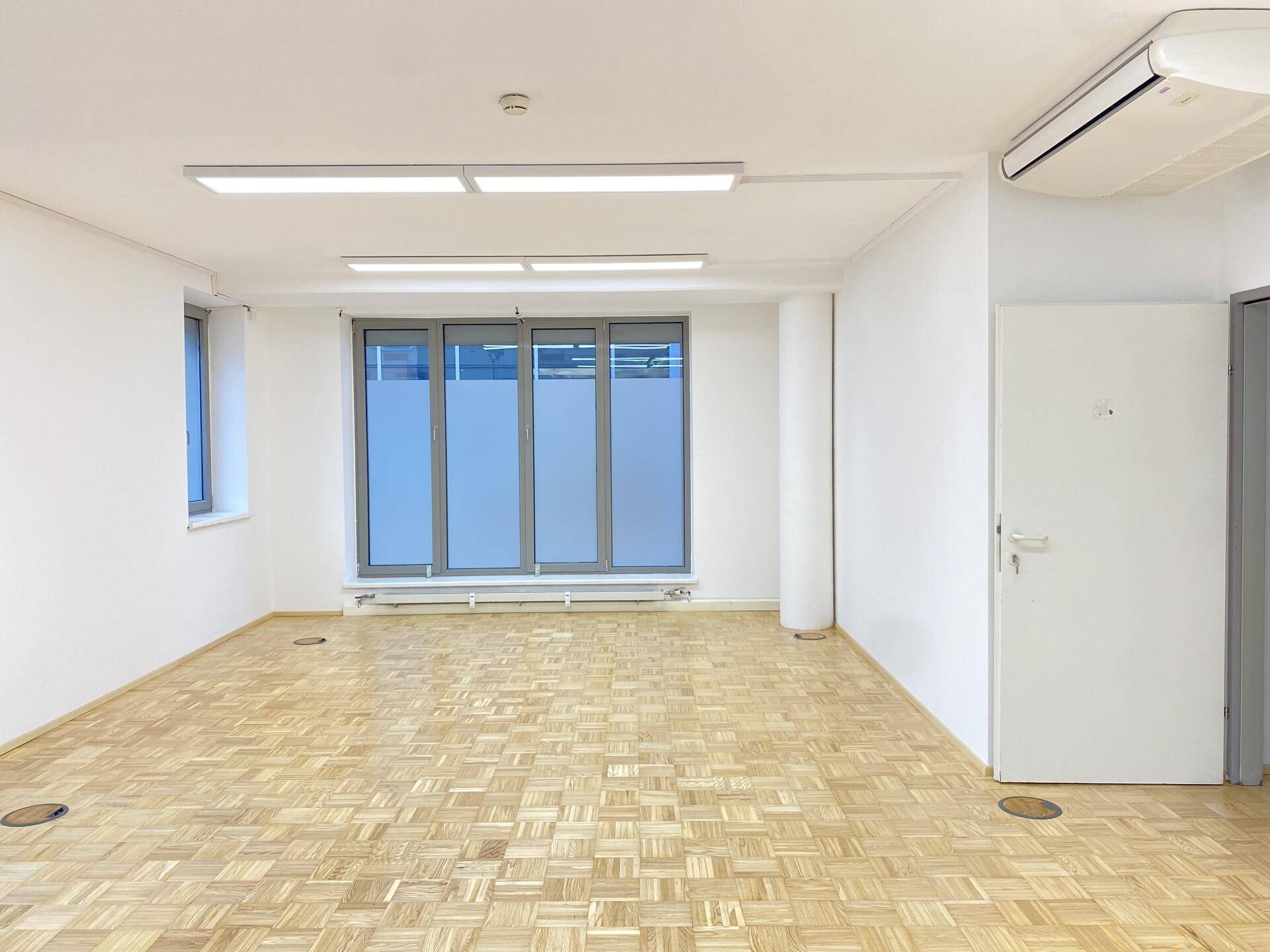 Helles Büro mit Parkettboden, Klimaanlage und großen Fenstern für viel Tageslicht.