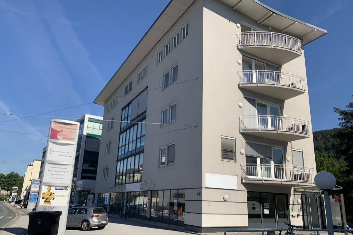 Modernes Geschäftsgebäude mit mehreren Balkonen und großen Fenstern unter blauem Himmel.