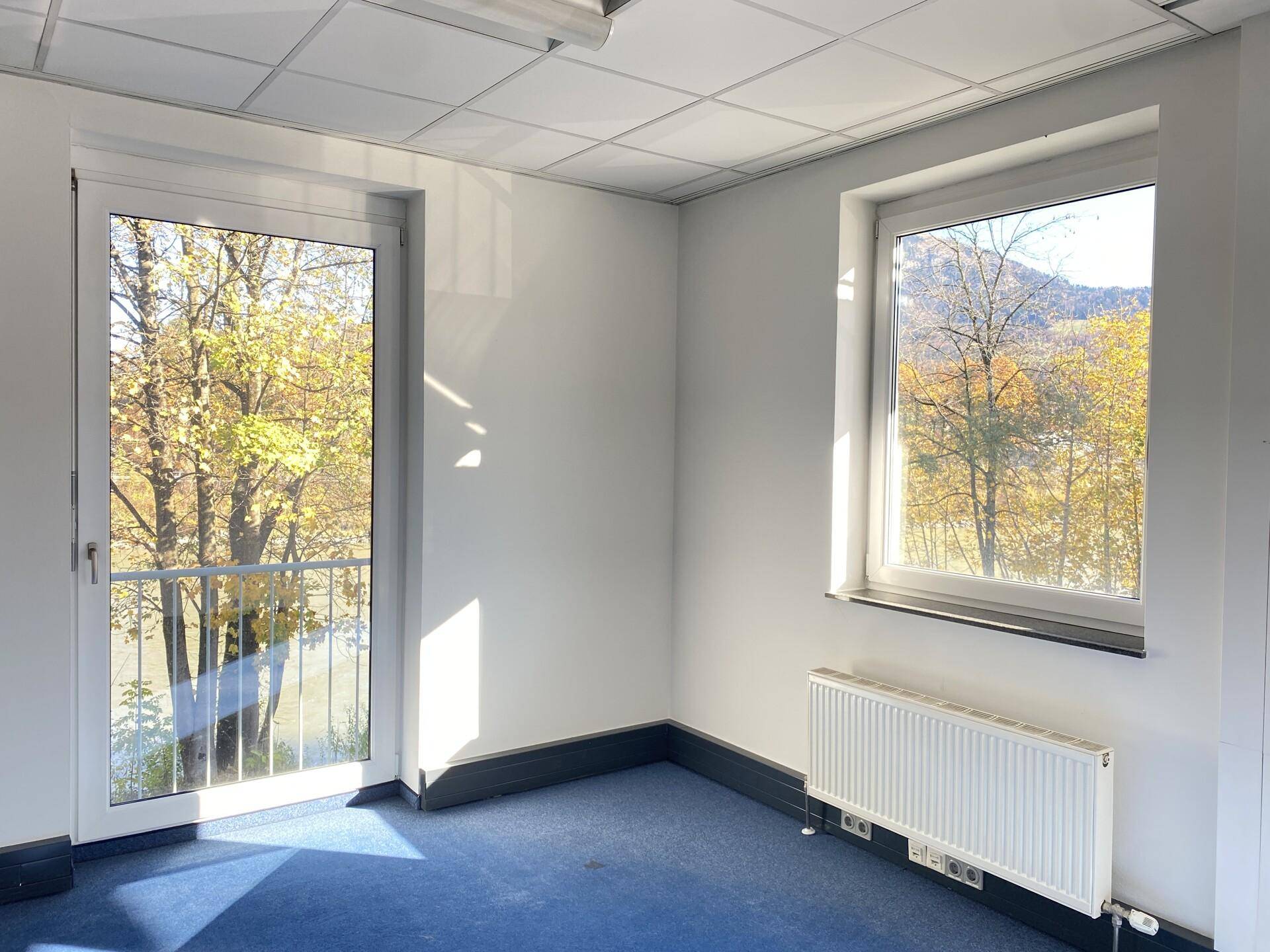 Helles Büro mit Teppichboden, Fenster und Zugang zu einem kleinen Balkon, mit Bergblick.