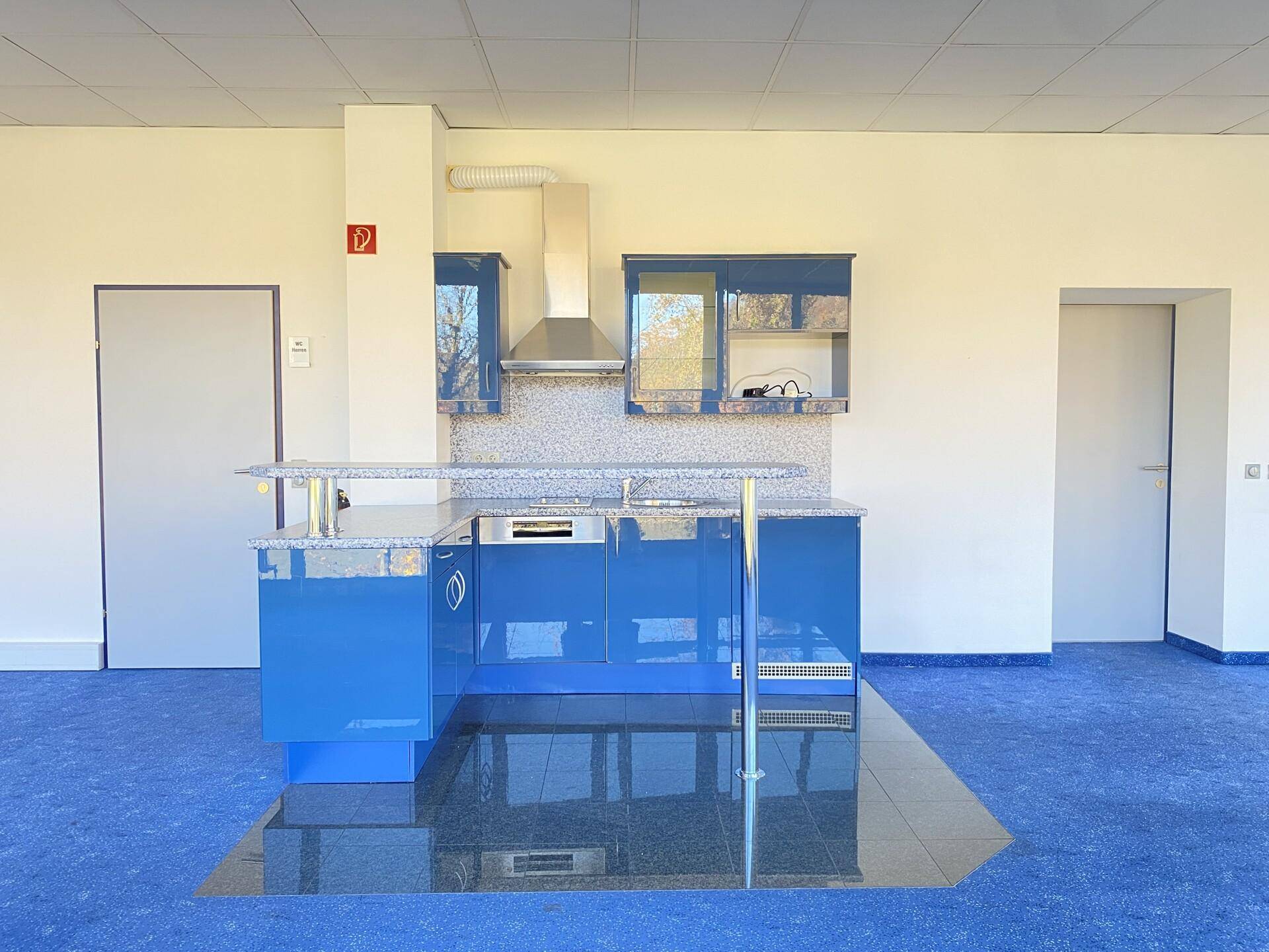 Moderne Küchenzeile mit blauen Hochglanzschränken, Granitarbeitsplatte und Dunstabzugshaube in einem Büro.