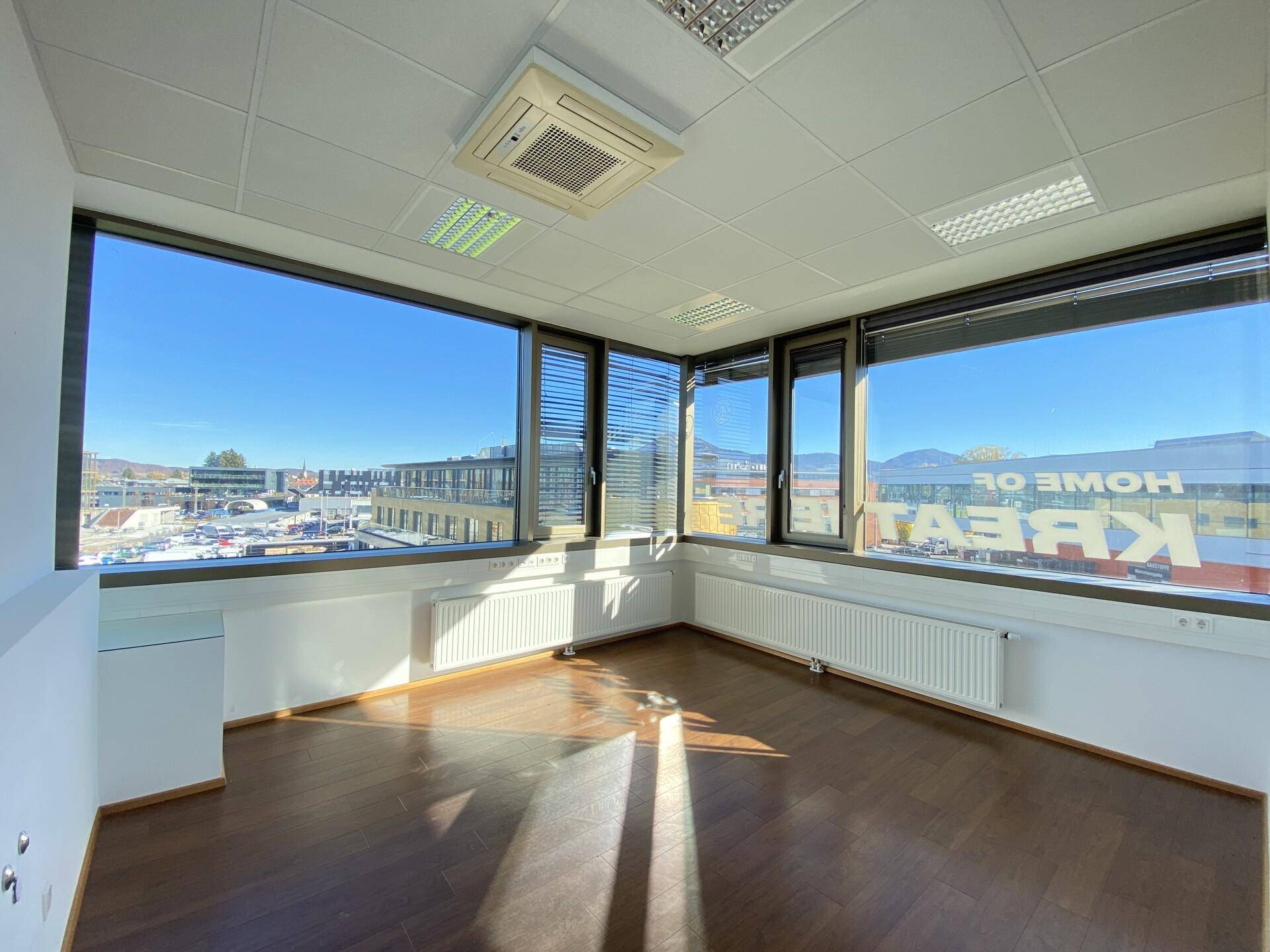Helles Büro mit Holzboden und großen Fenstern, die einen weiten Blick auf die Stadt und die Umgebung bieten.