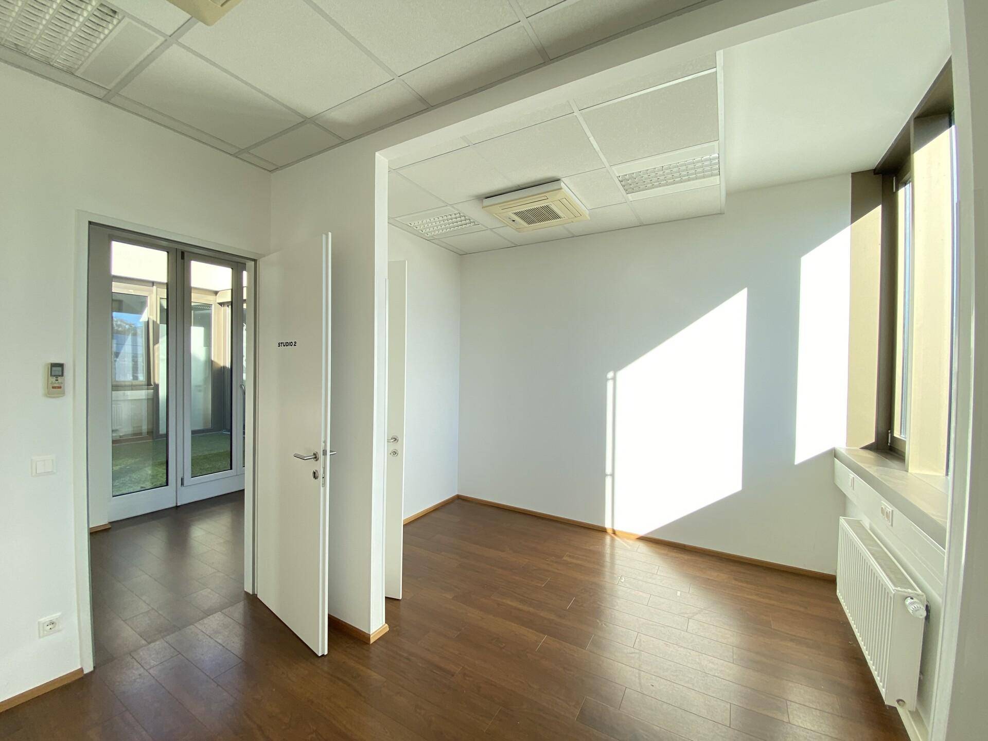 Helles, leeres Büro mit Holzboden und Zugang zu einem Atrium durch eine Glastür.
