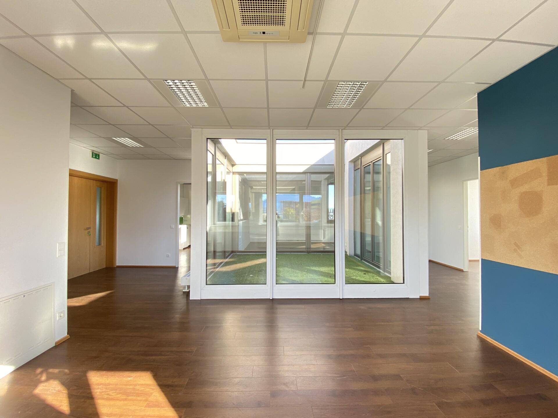 Helles Büro mit Holzboden und großen Glasfronten, die einen Blick auf ein begrüntes Atrium bieten.
