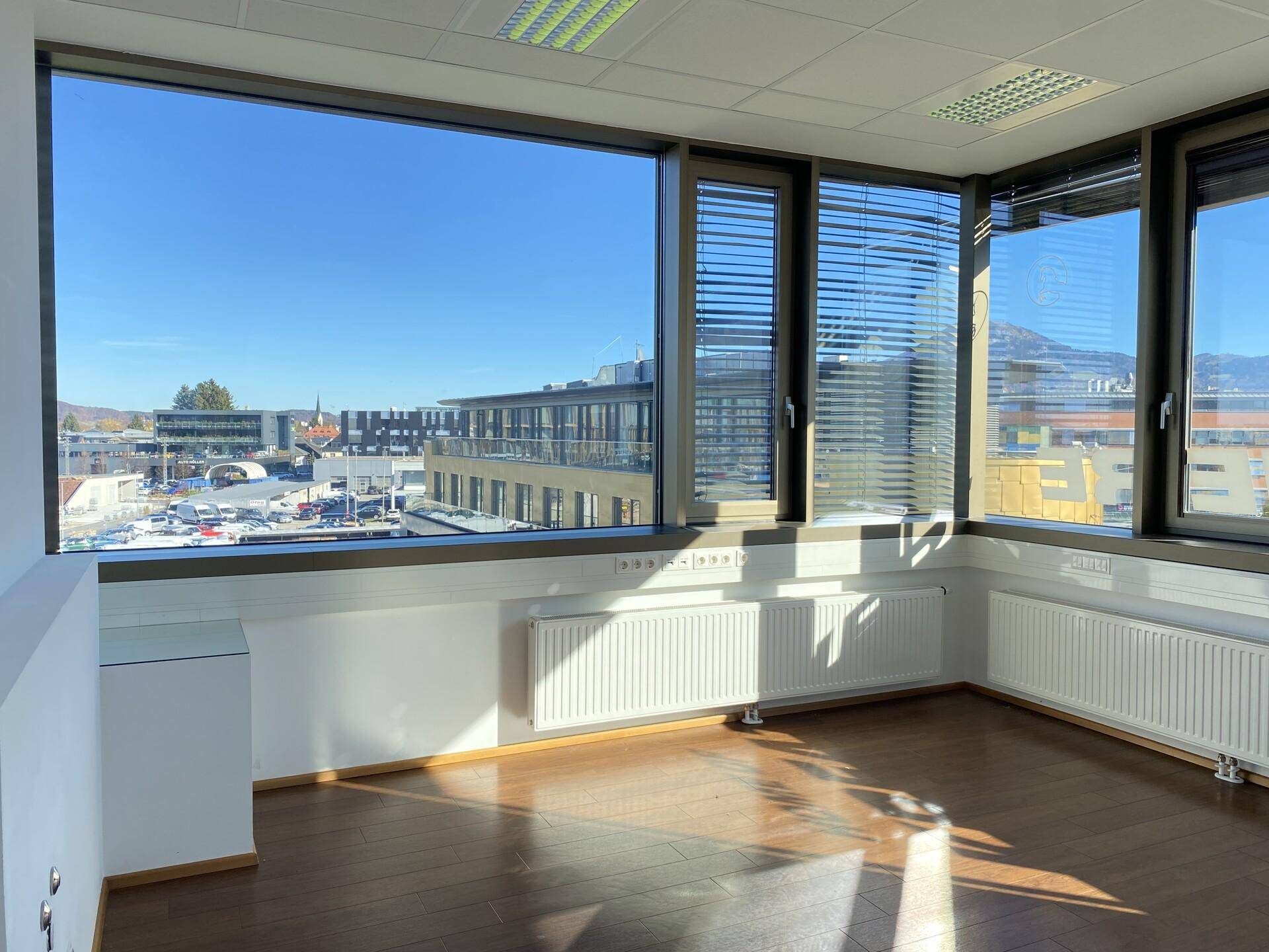 Geräumiges Büro mit Holzboden und großen Fenstern, die einen Panoramablick auf die städtische Umgebung bieten.