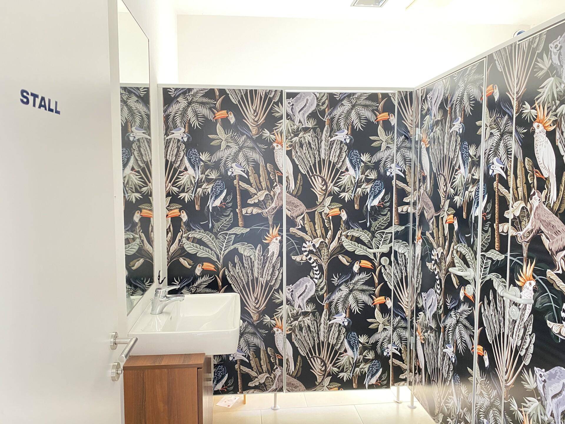 Toilettenbereich mit mehreren Kabinen, die mit einem auffälligen tropischen Muster dekoriert sind.