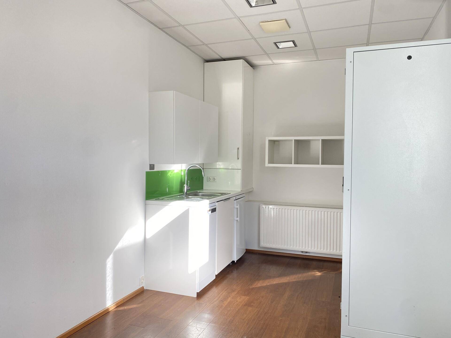 Kleine, funktionale Küchenzeile mit weißen Schränken, Spüle und grünem Spritzschutz.