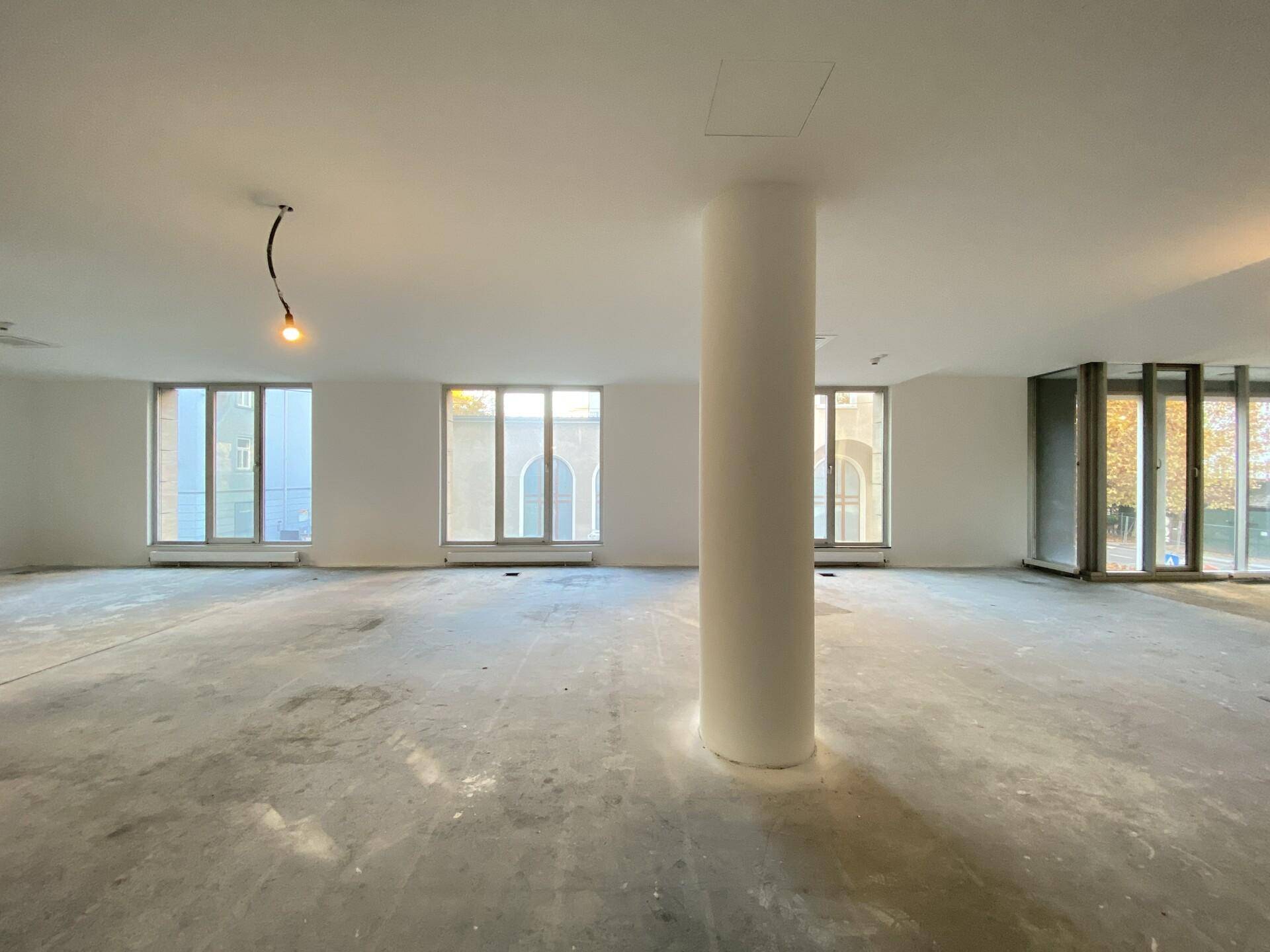 Offener Bürobereich mit zentraler Säule, großen Fenstern und viel natürlichem Licht, schafft eine helle Arbeitsumgebung.