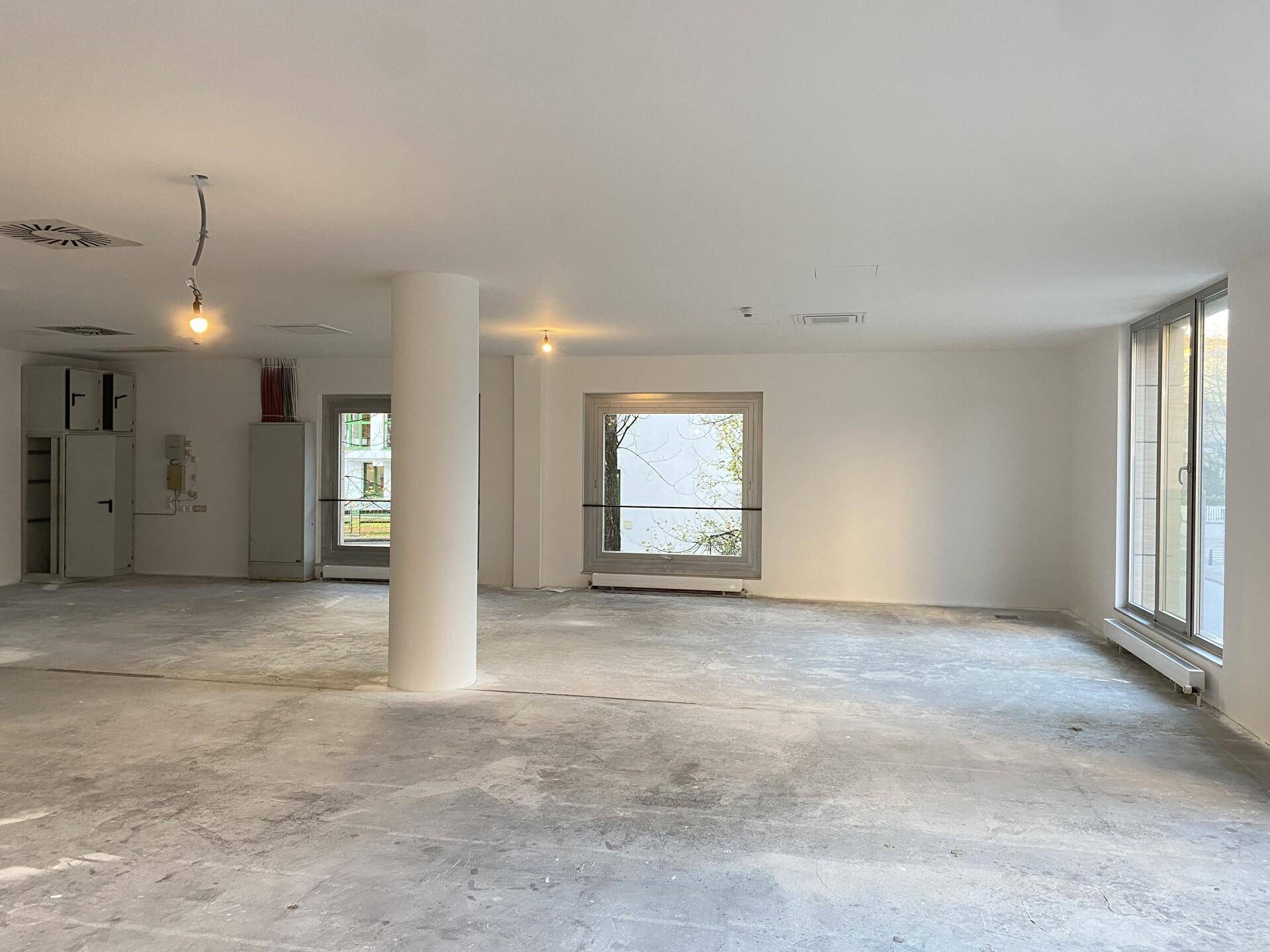 Geräumiger Büroraum mit Betonboden, großen Fenstern und vorbereiteten Installationen, bereit für den Ausbau.
