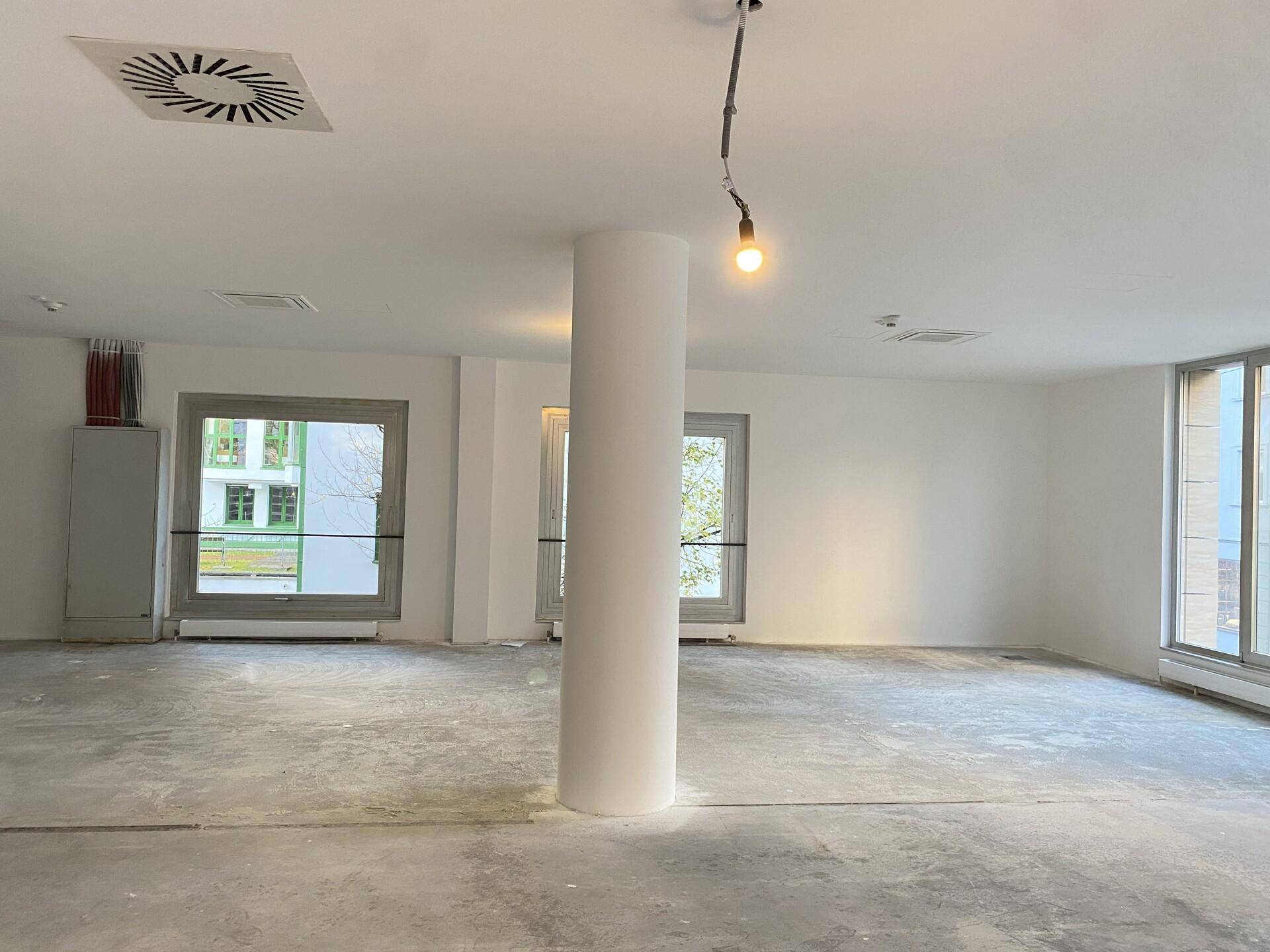 Heller Büroraum mit Betonboden, Deckenlüftung und vorbereiteten Anschlüssen für die Einrichtung, modern und funktional.