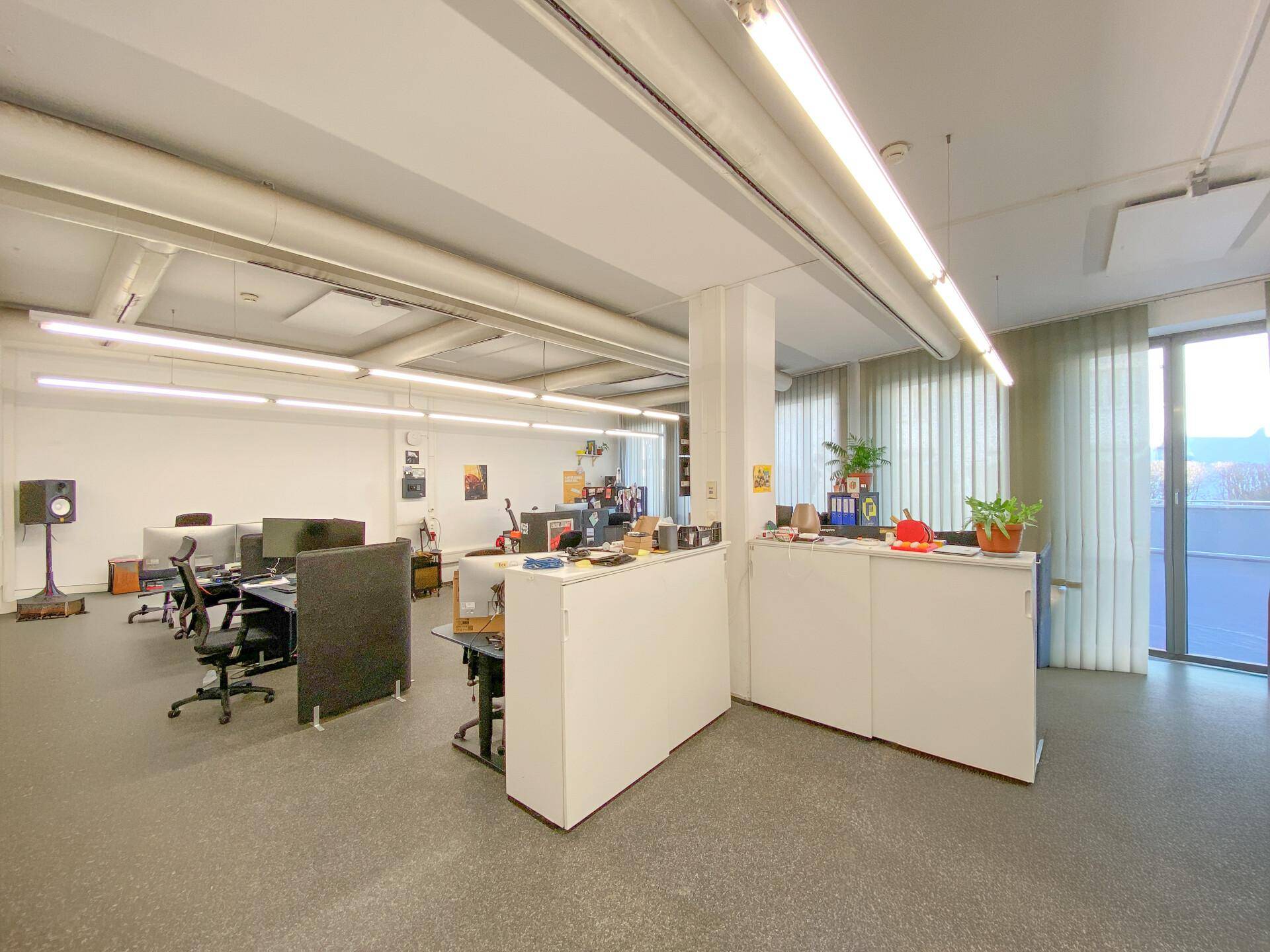 Großes, offenes Büro mit zahlreichen Arbeitsplätzen, modernen Möbeln und viel natürlichem Licht durch die Fenster.