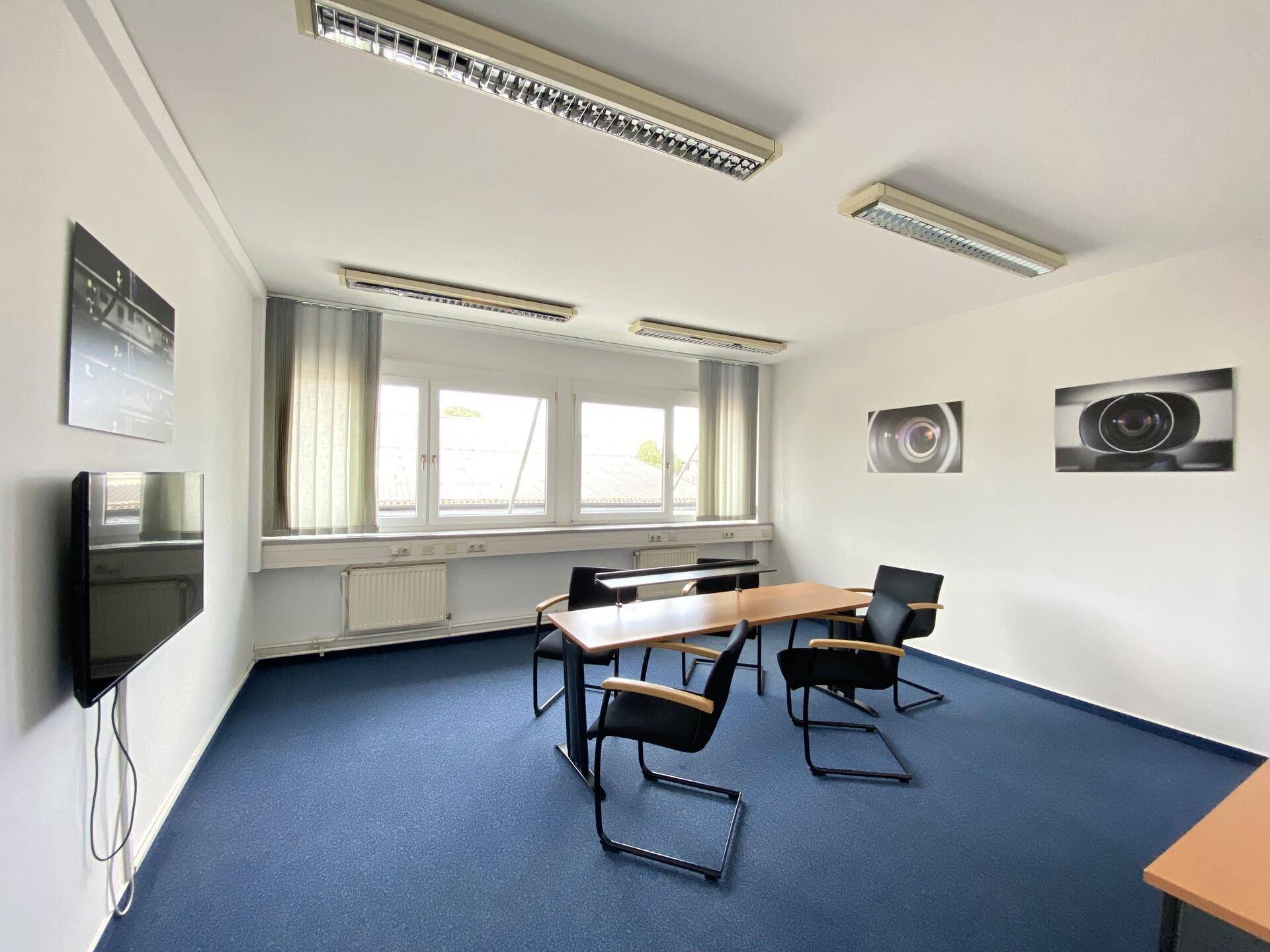 Kleiner Besprechungsbereich mit Tisch, Stühlen und Wandfernseher, ideal für informelle Treffen.