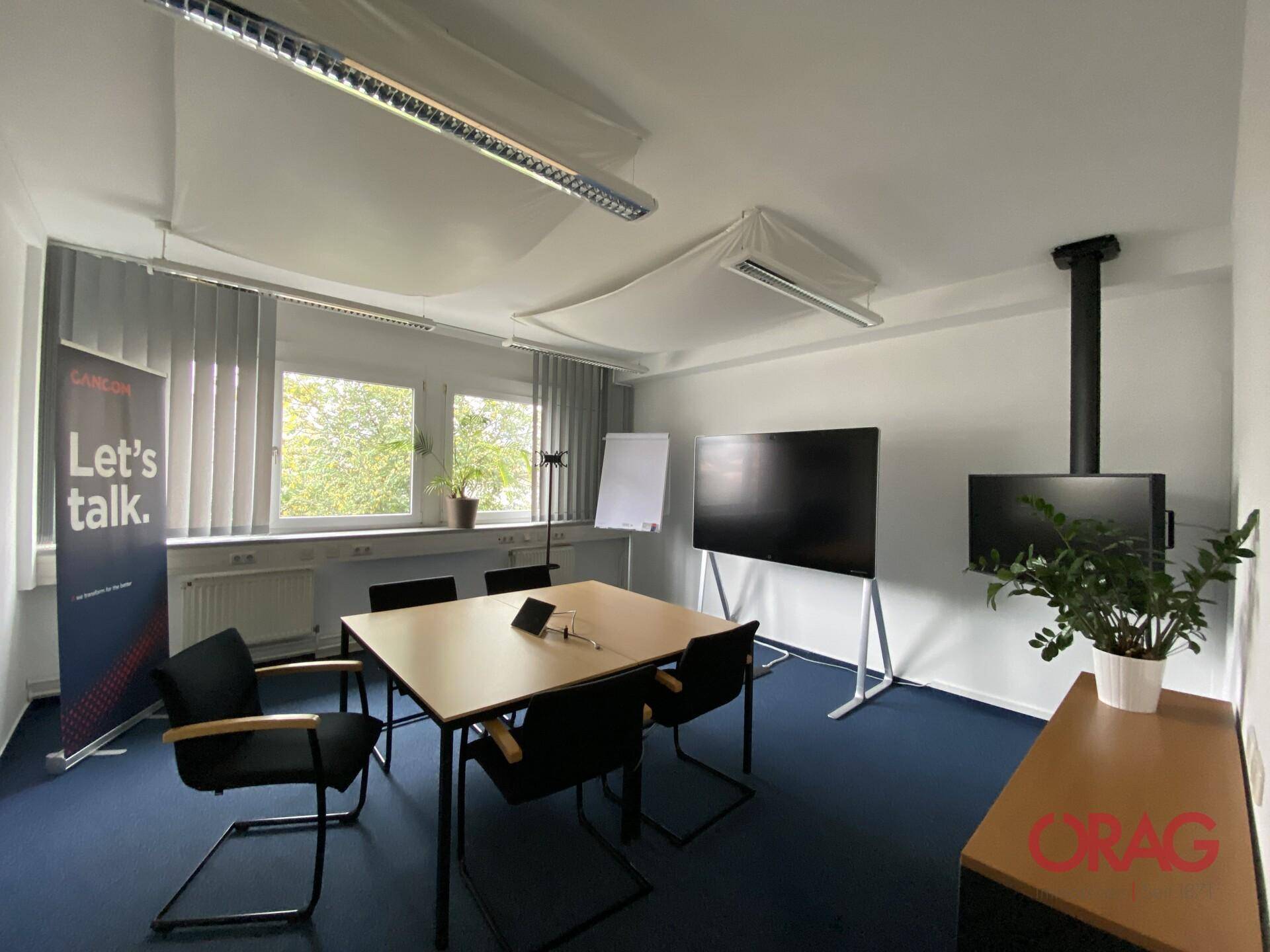 Kleiner Besprechungsraum mit Tisch, Stühlen, Whiteboard und zwei Bildschirmen, ideal für Team-Meetings.