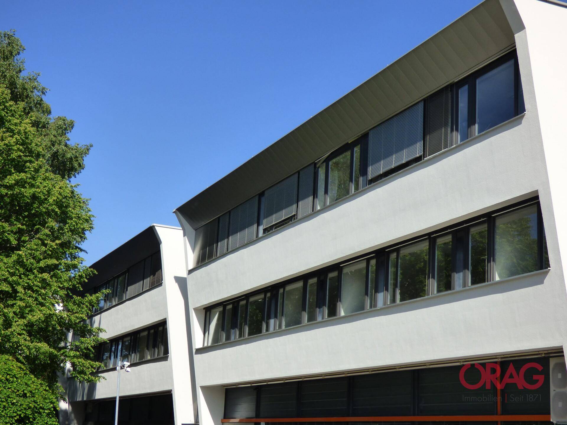 Moderne Bürogebäude-Fassade mit großen Fensterfronten und klarem blauen Himmel im Hintergrund.