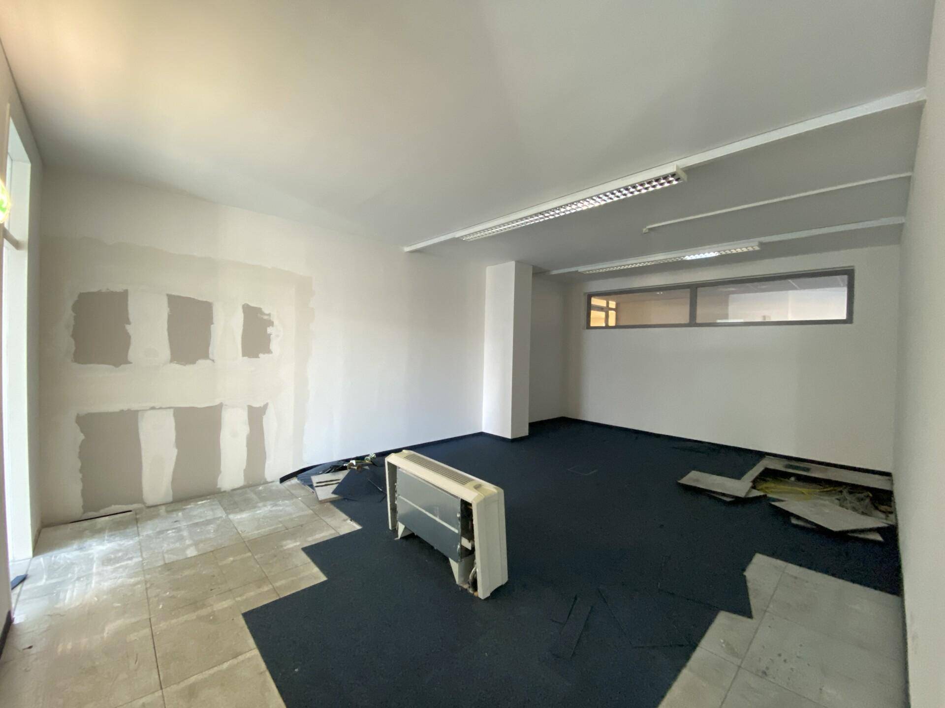 Büroraum in Renovierung mit teilweise entferntem Teppichboden und sichtbaren Wandreparaturen.
