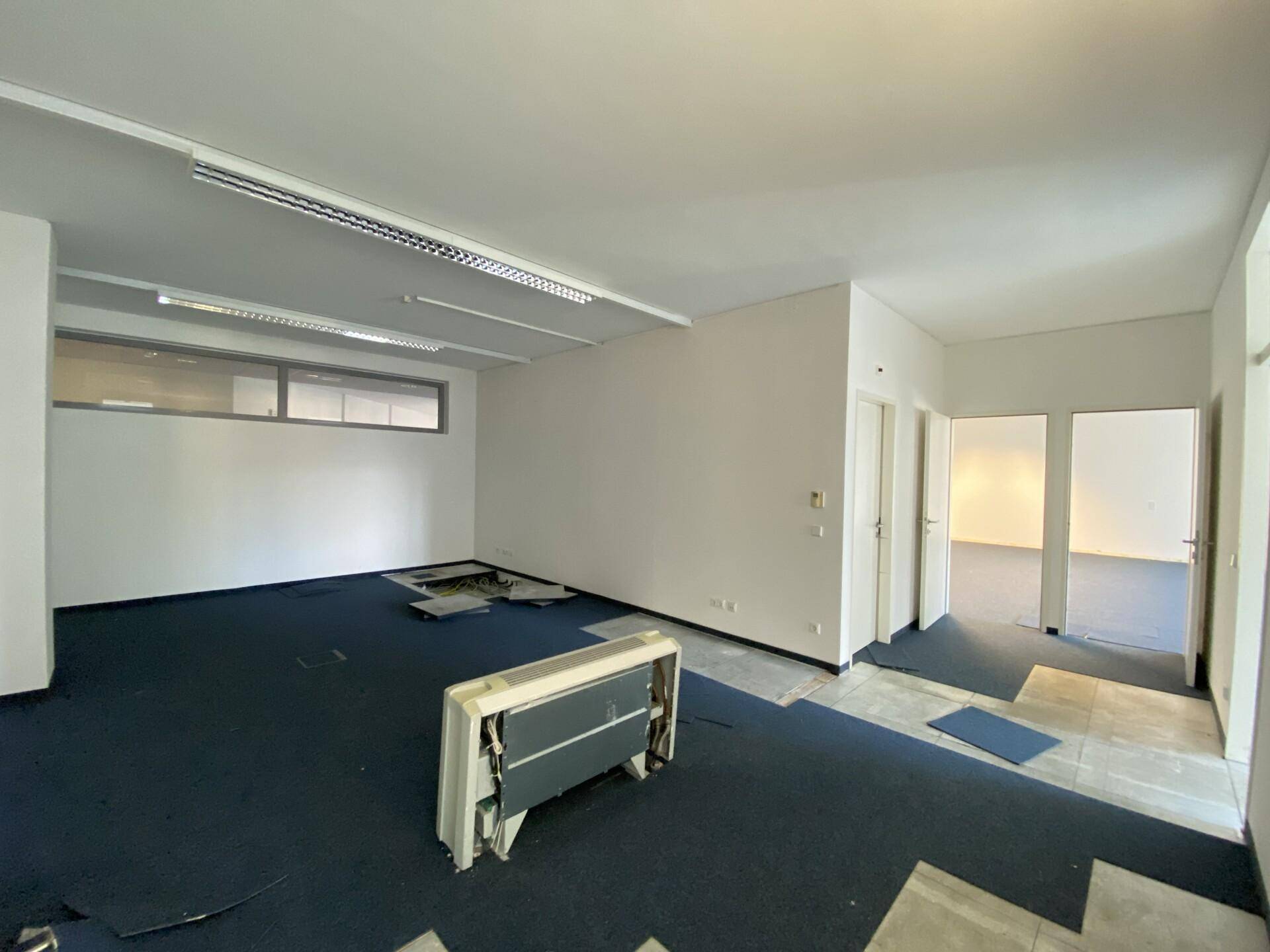 Büroraum in Renovierung mit unterschiedlichen Bodenbelägen und sichtbaren Installationsarbeiten.