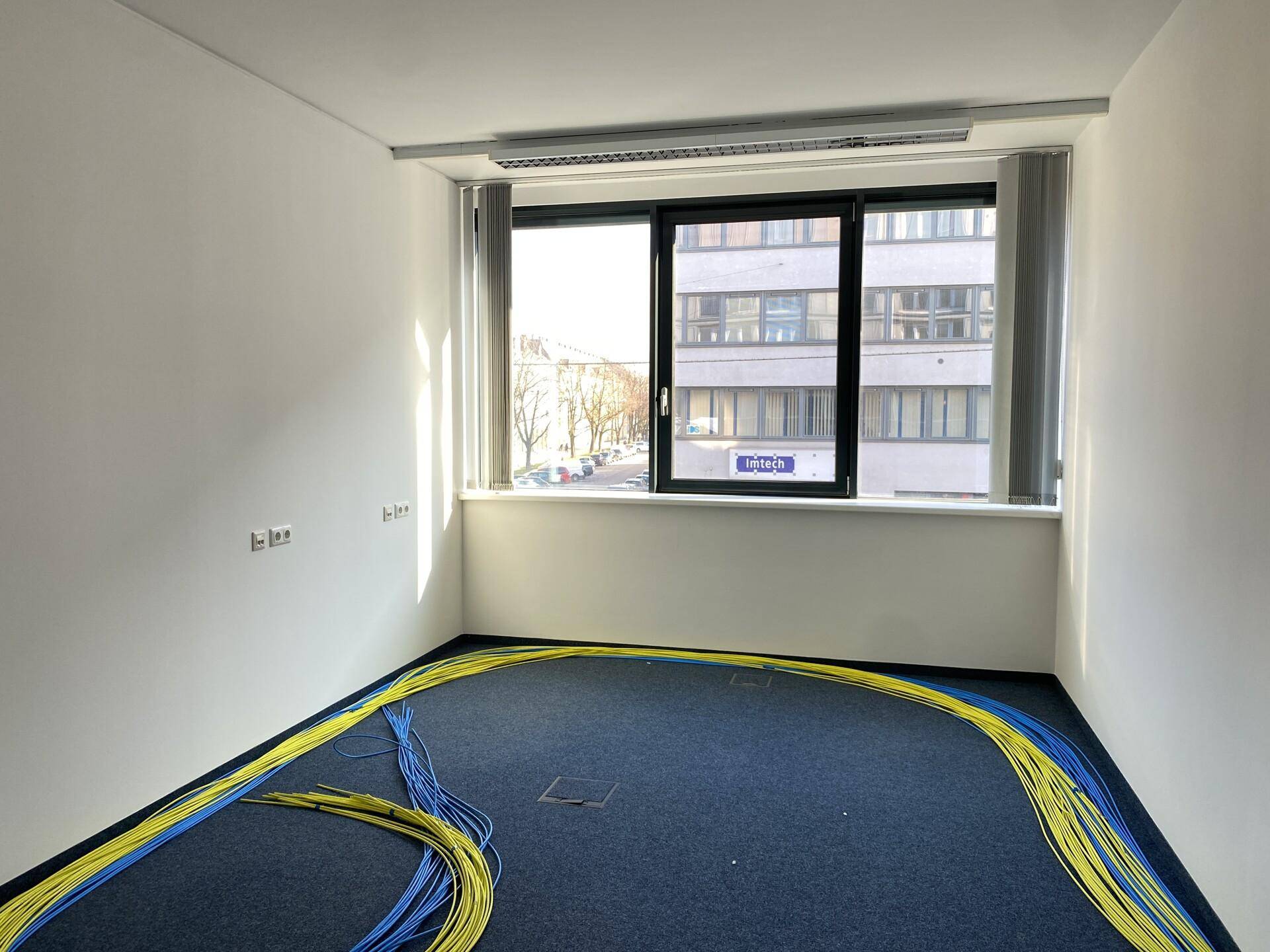 Büroraum mit blauem Teppichboden und zahlreichen Kabeln, die auf die Installation warten.