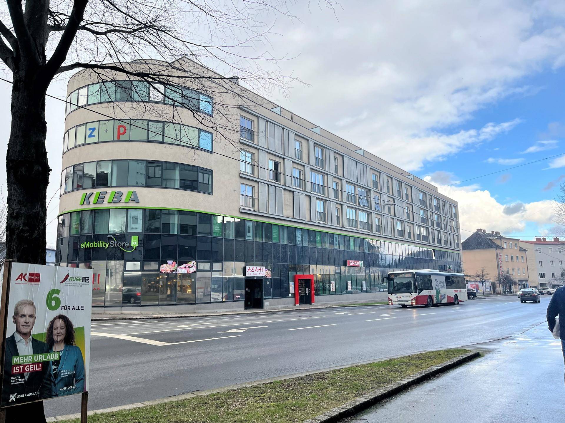 Modernes Geschäftsgebäude mit Glasfassade und Geschäften im Erdgeschoss an einer belebten Straße.