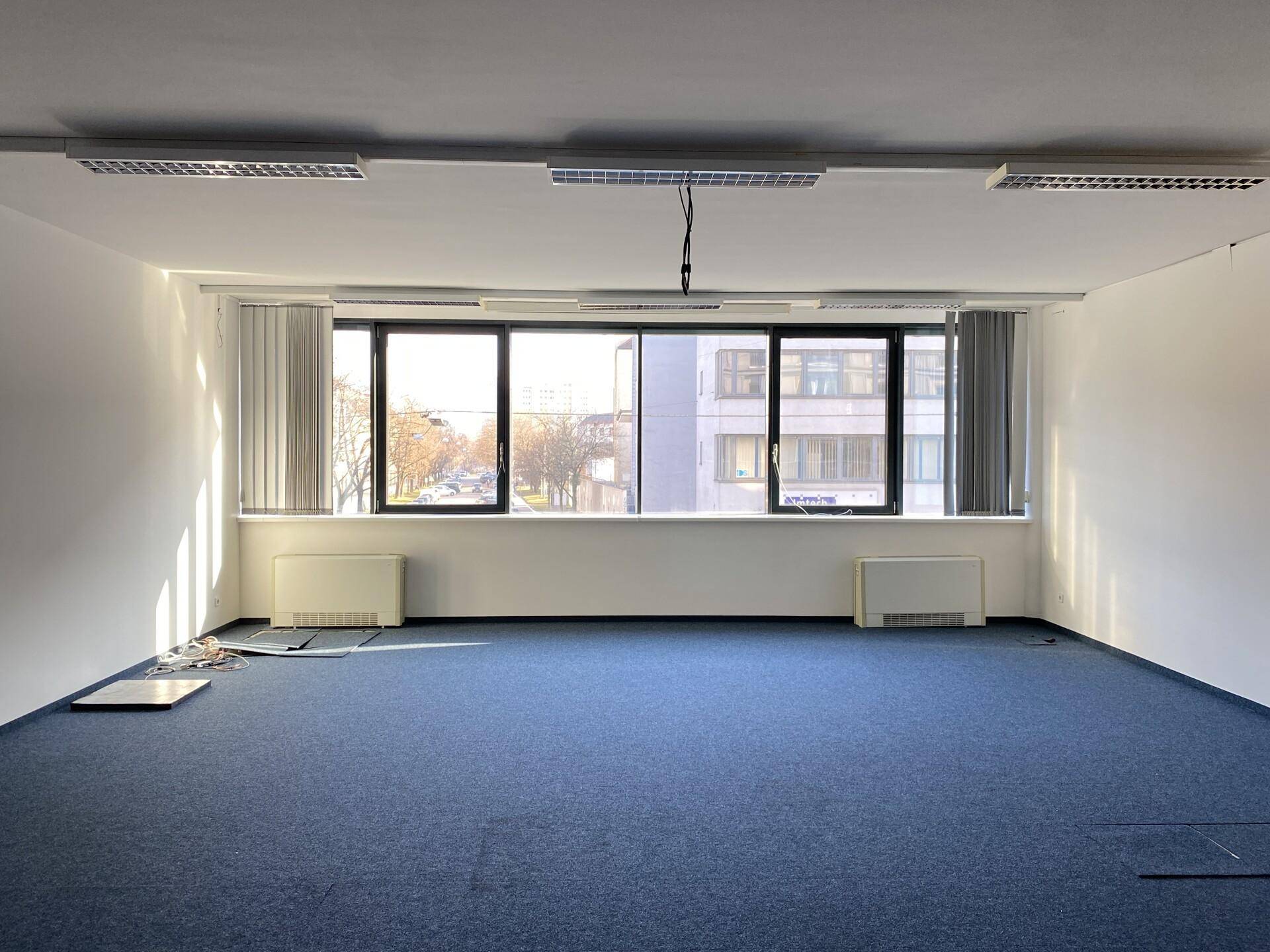Heller Büroraum mit großen Fenstern und Blick auf die umliegenden Gebäude, ausgestattet mit Heizkörpern.