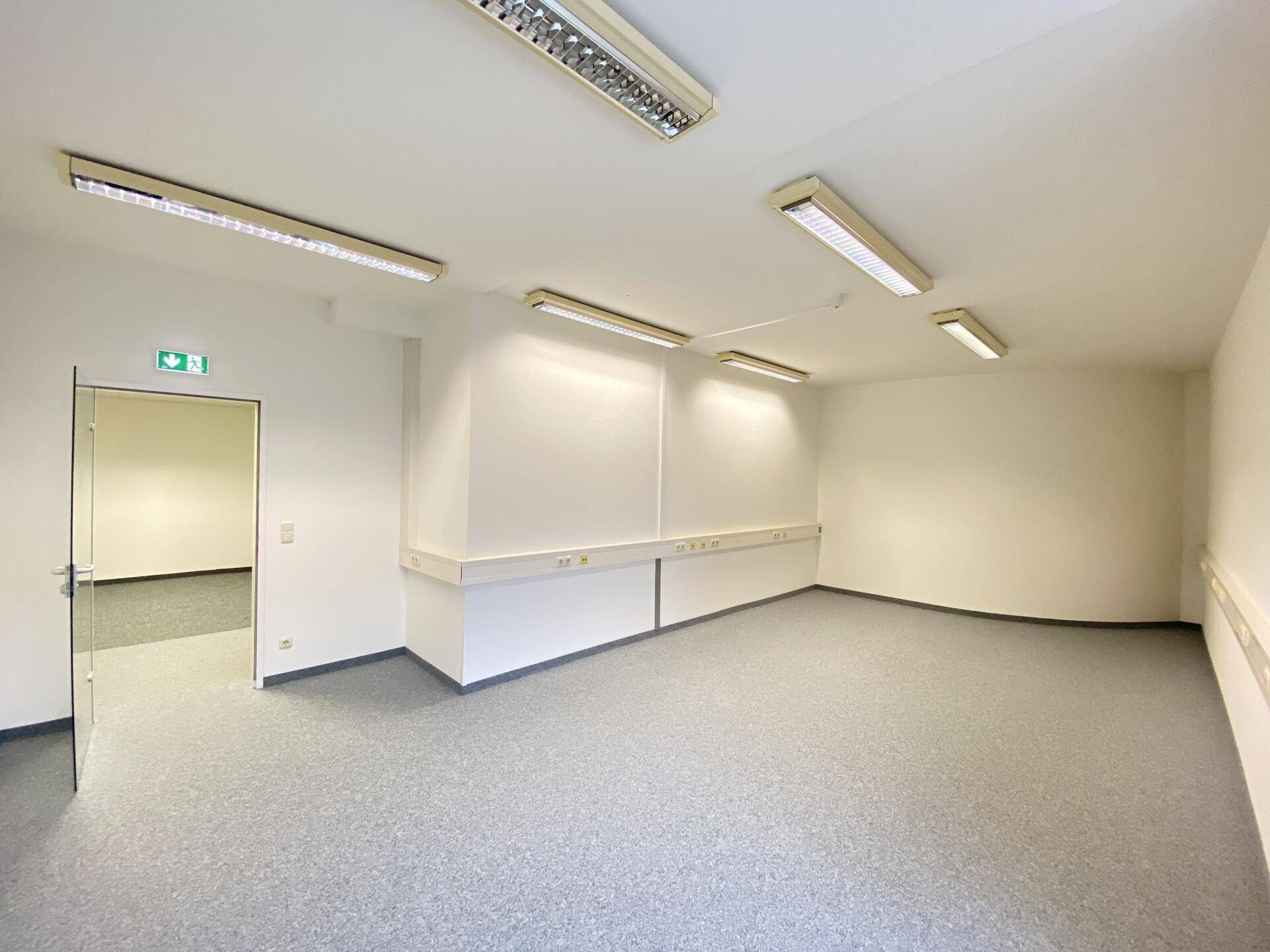 Leeres Büro mit Teppichboden und einer Glastür, die zu einem weiteren Raum führt, ideal für flexible Nutzung.
