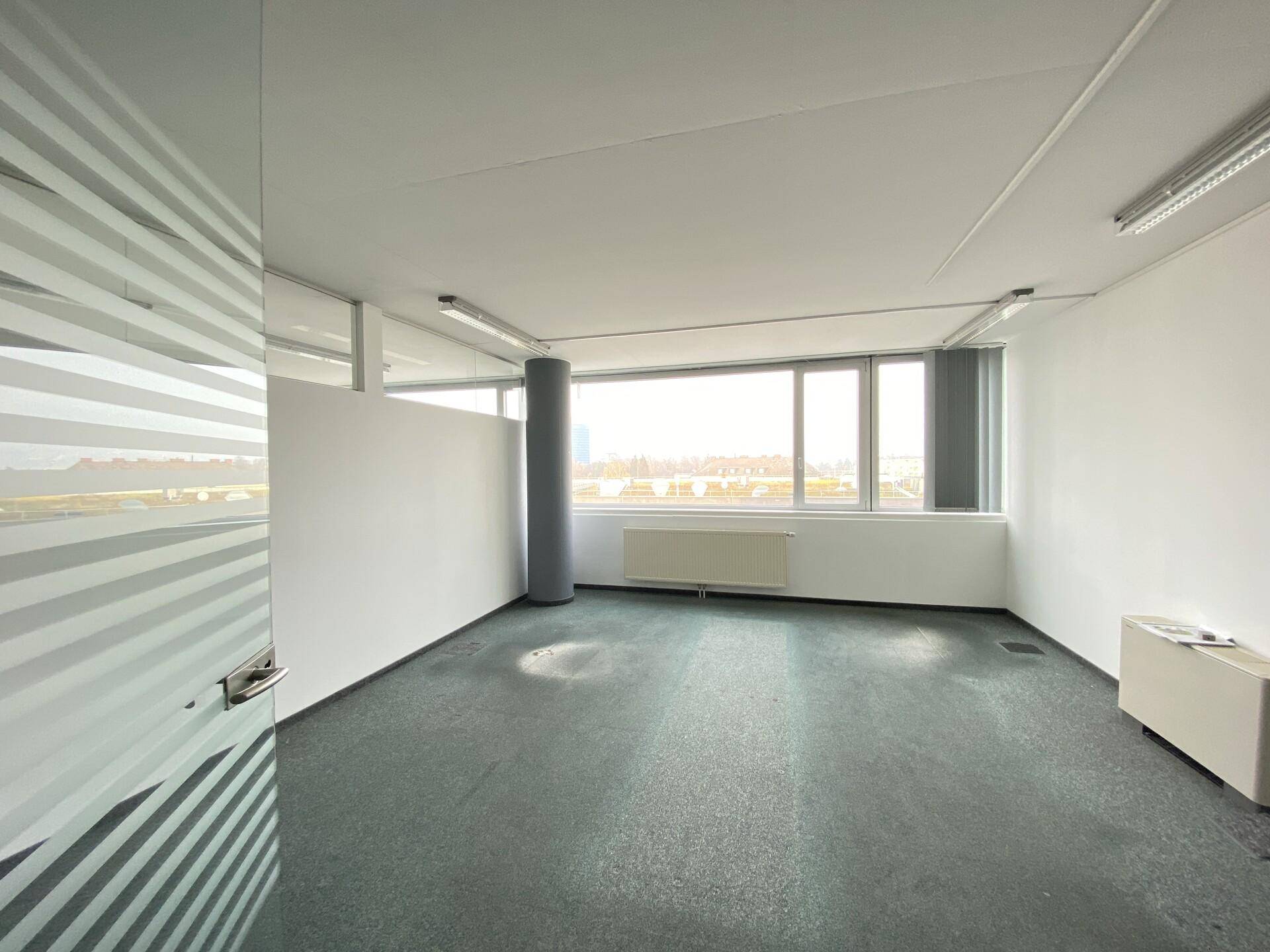 Leerer Büroraum mit Teppichboden und Fenster, bietet einen weiten Blick über die Umgebung.