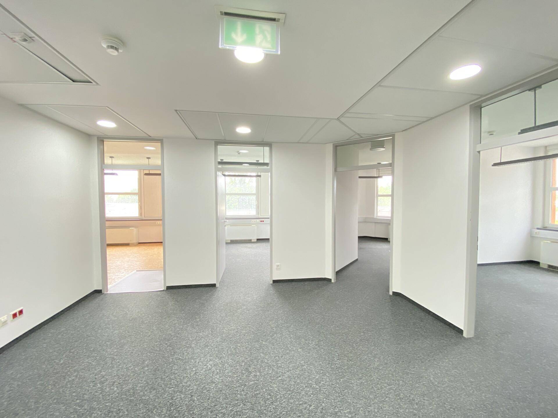 Heller Bürogang mit mehreren Türen zu Büroräumen und einem Fluchtwegschild.