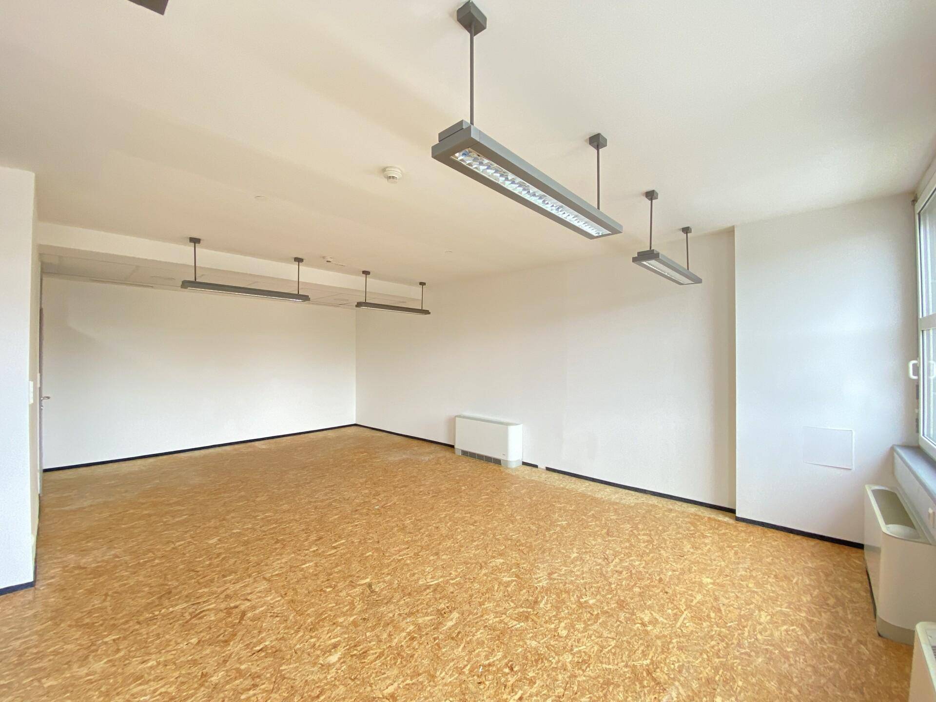 Helles Büro mit OSB-Plattenboden, weißen Wänden und modernen Deckenleuchten.