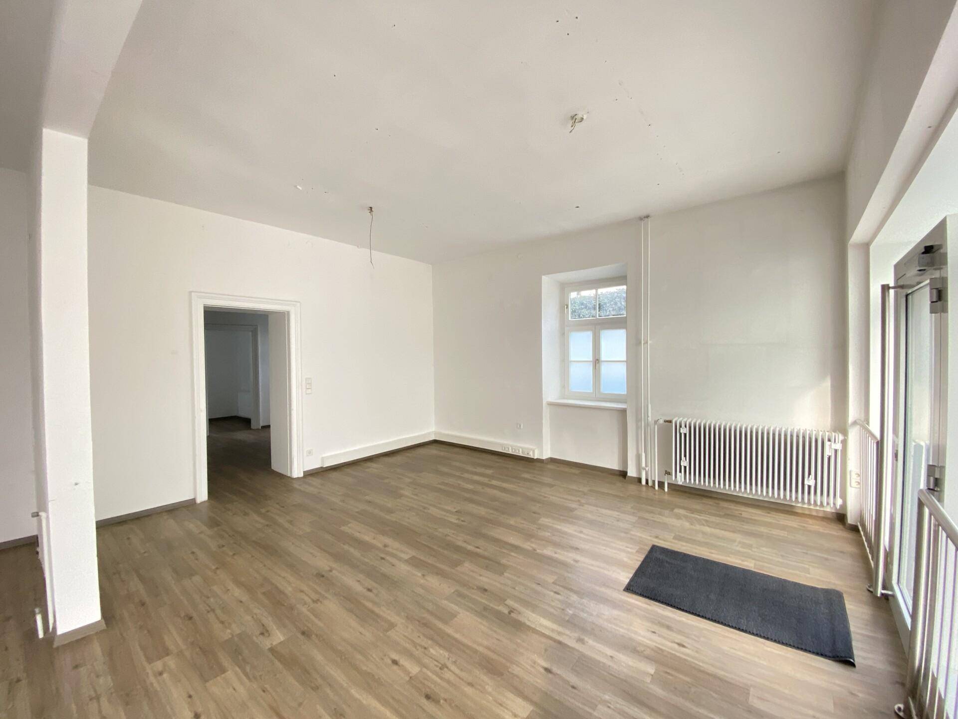 Innenansicht eines Gewerberaums mit Laminatboden, weiß gestrichenen Wänden und einem Fenster.