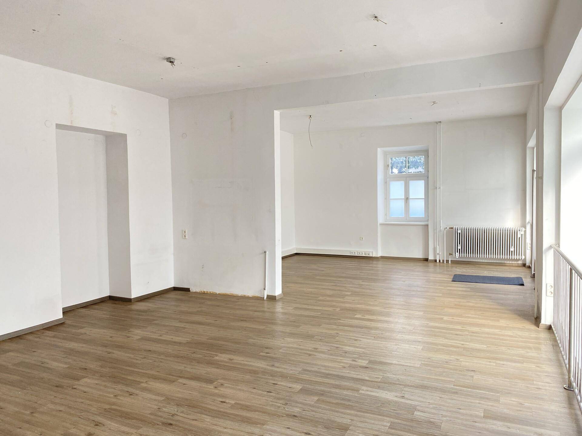 Weitläufiger Gewerberaum mit Laminatboden und mehreren Fenstern, bereit zur individuellen Gestaltung.
