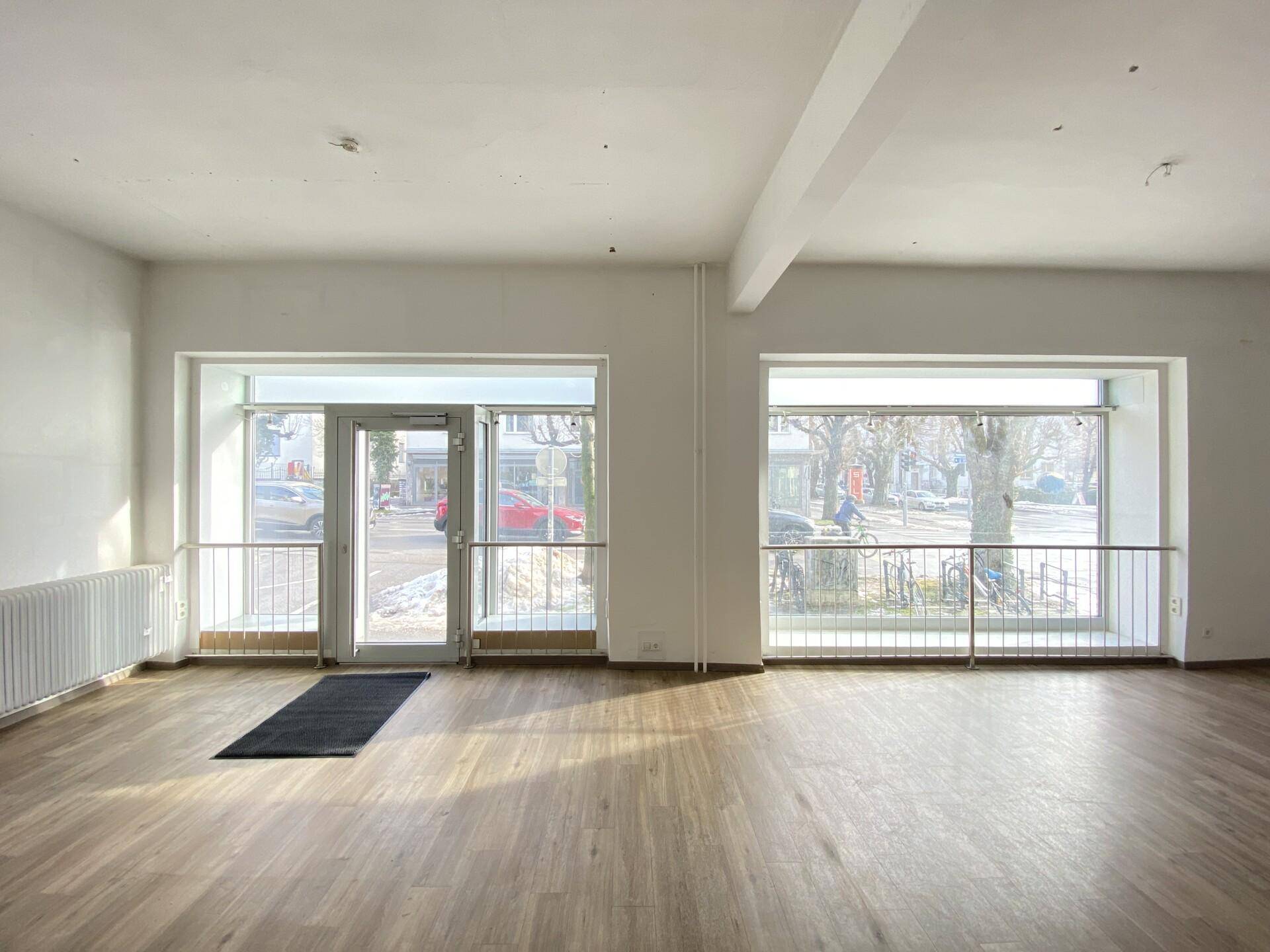 Heller Gewerberaum mit großen Schaufenstern zur Straße und modernem Laminatboden.