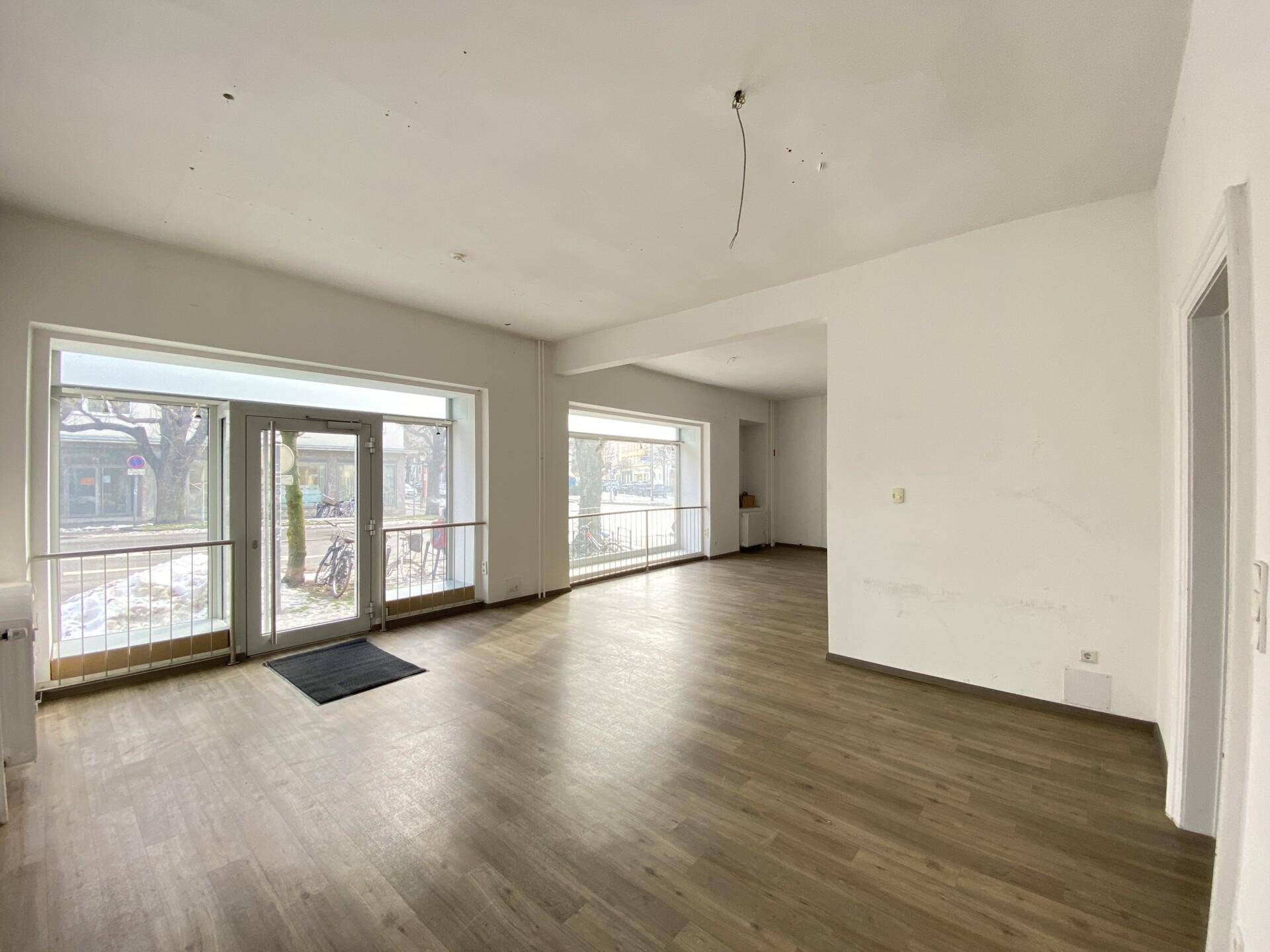 Geräumiger Gewerberaum mit großen Schaufenstern und Laminatboden, ideal für Kundenverkehr.