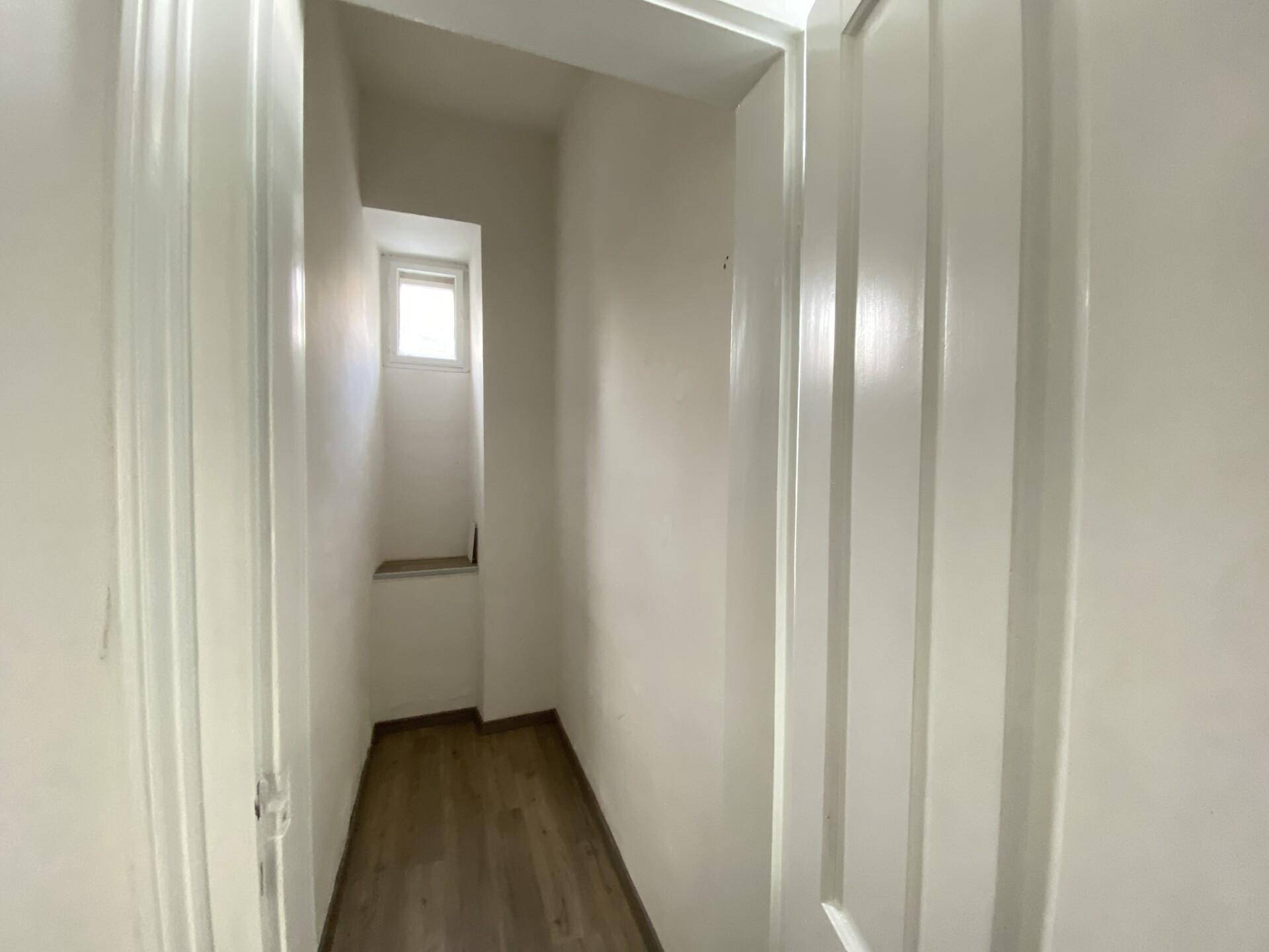 Schmaler Flur oder Abstellraum mit kleinem Fenster und Laminatboden, hell gestrichen.
